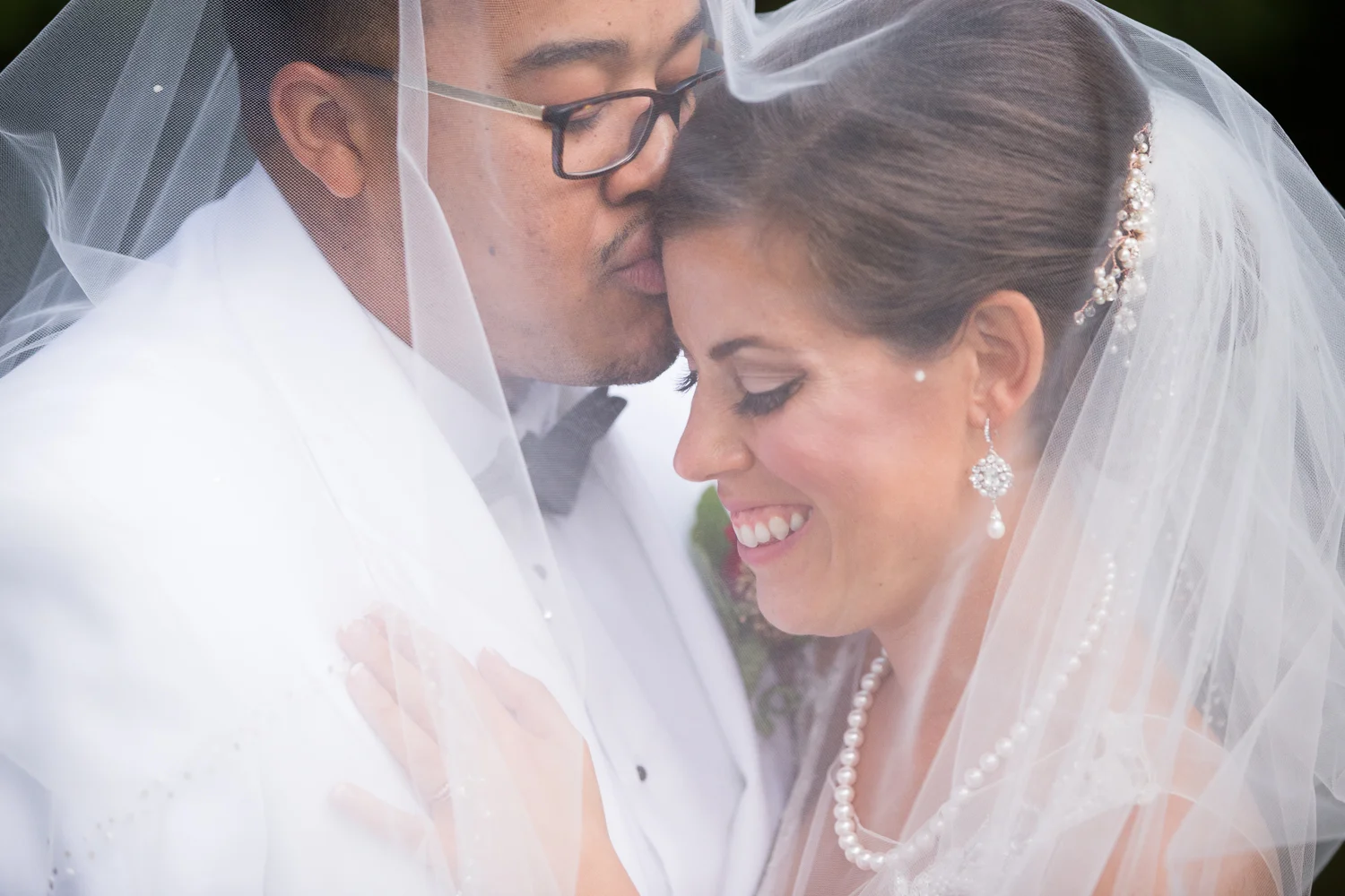 Groom kissing bride's forehead under wedding veil