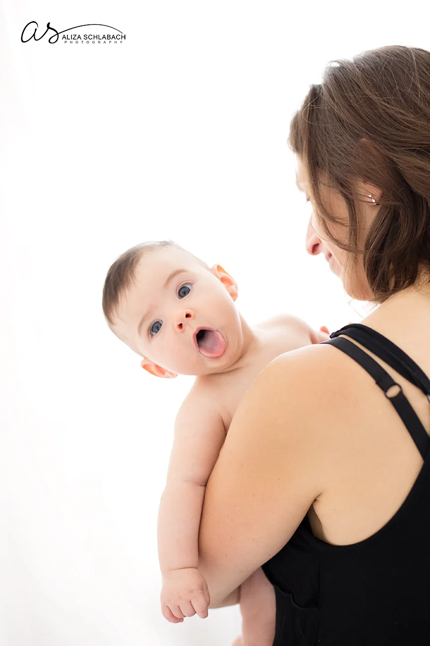 Backlit photo of a baby peaking over his mother's shoulder
