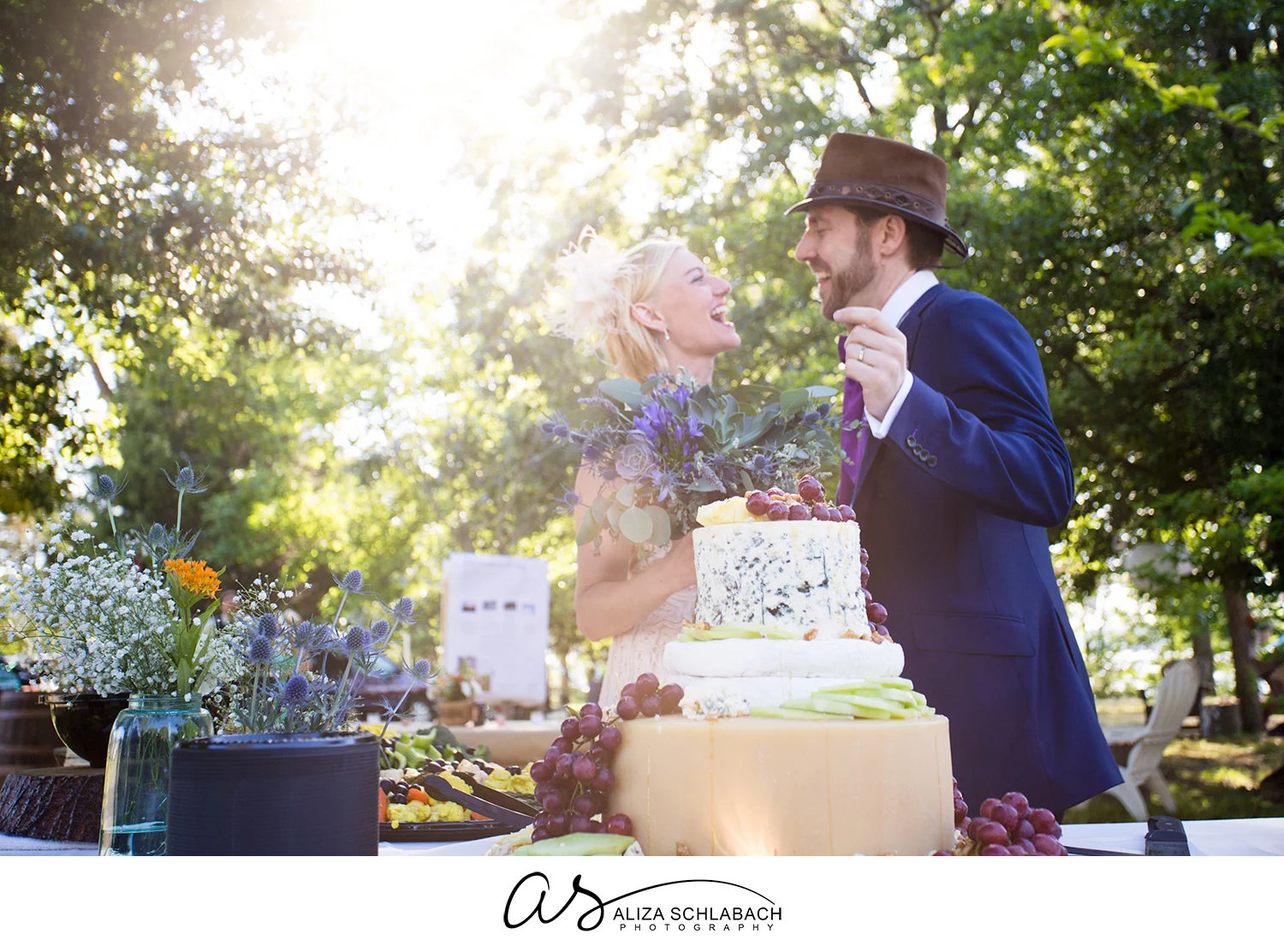 Backlit photo of bride and groom behind their wedding cake make of wheels of cheese