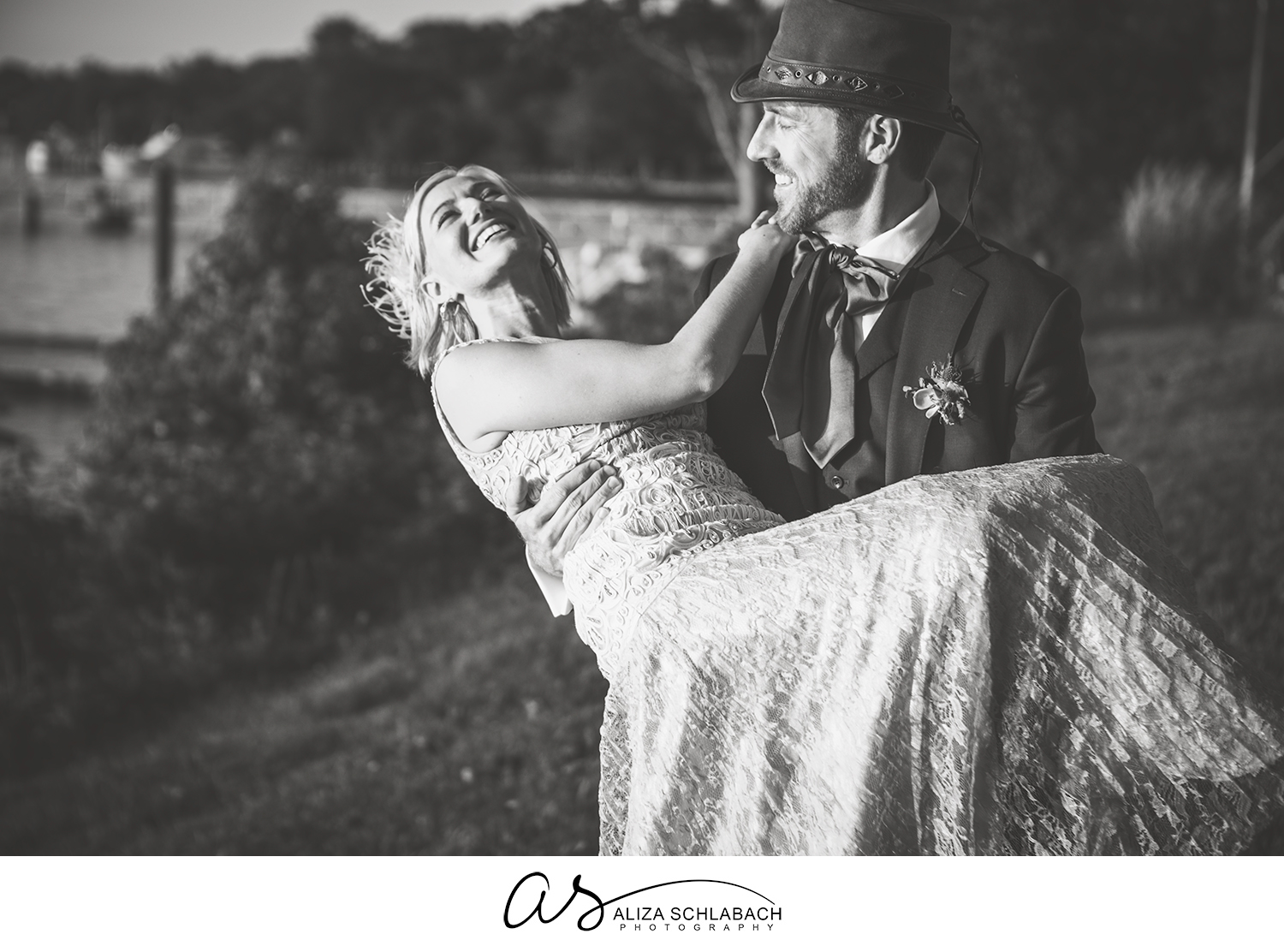 Black and white photo of a groom carrying his laughing bride