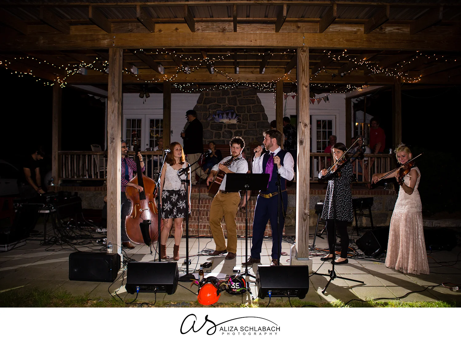 Backlit photo of bride and groom joining band during wedding reception