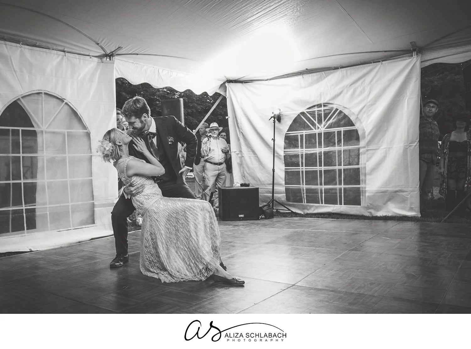 Black and white photograph of groom dipping his bride during their first dance in a tent
