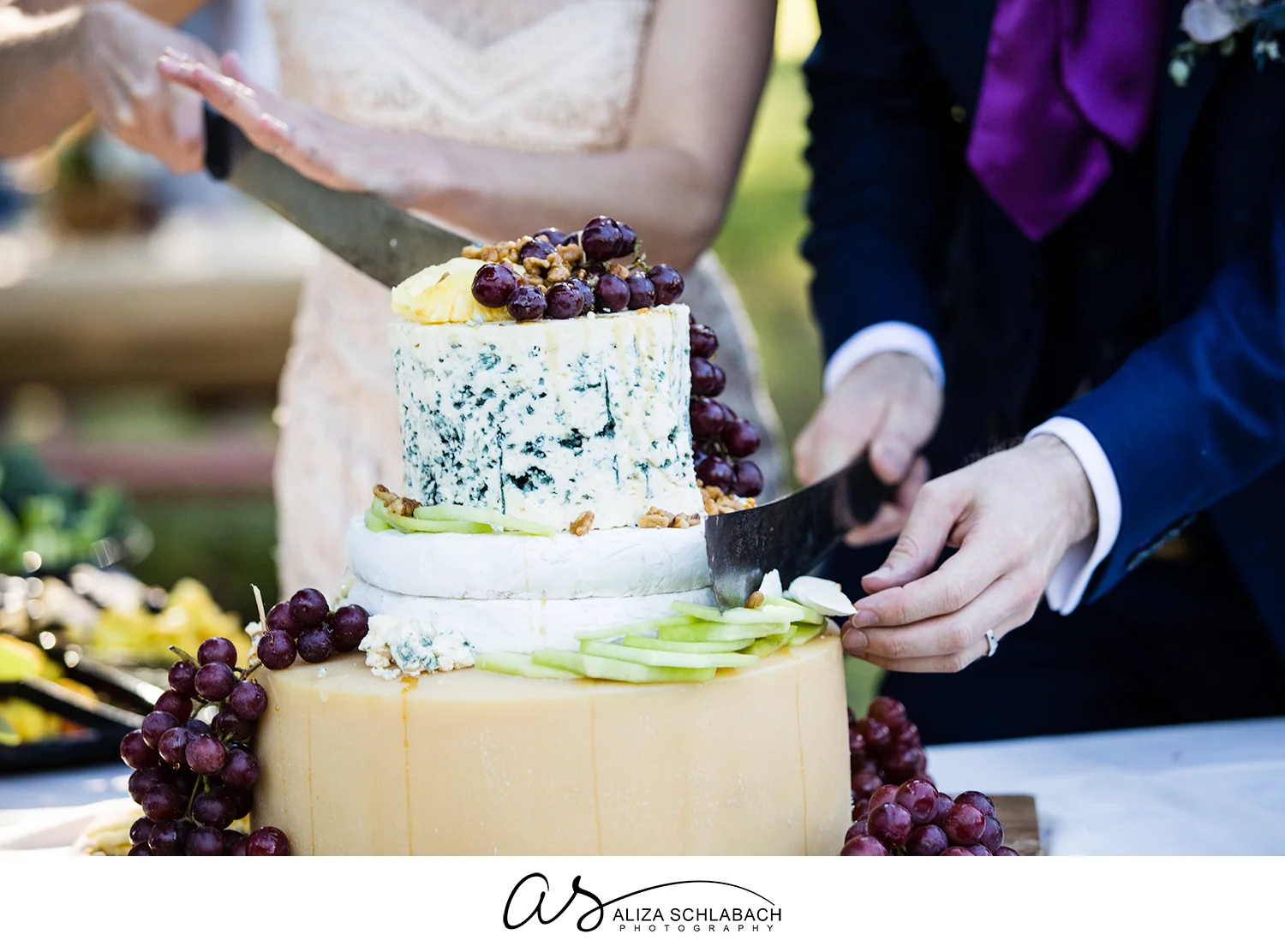 Close up photograph of bride and groom cutting their wedding cake, which is made of wheels of cheese