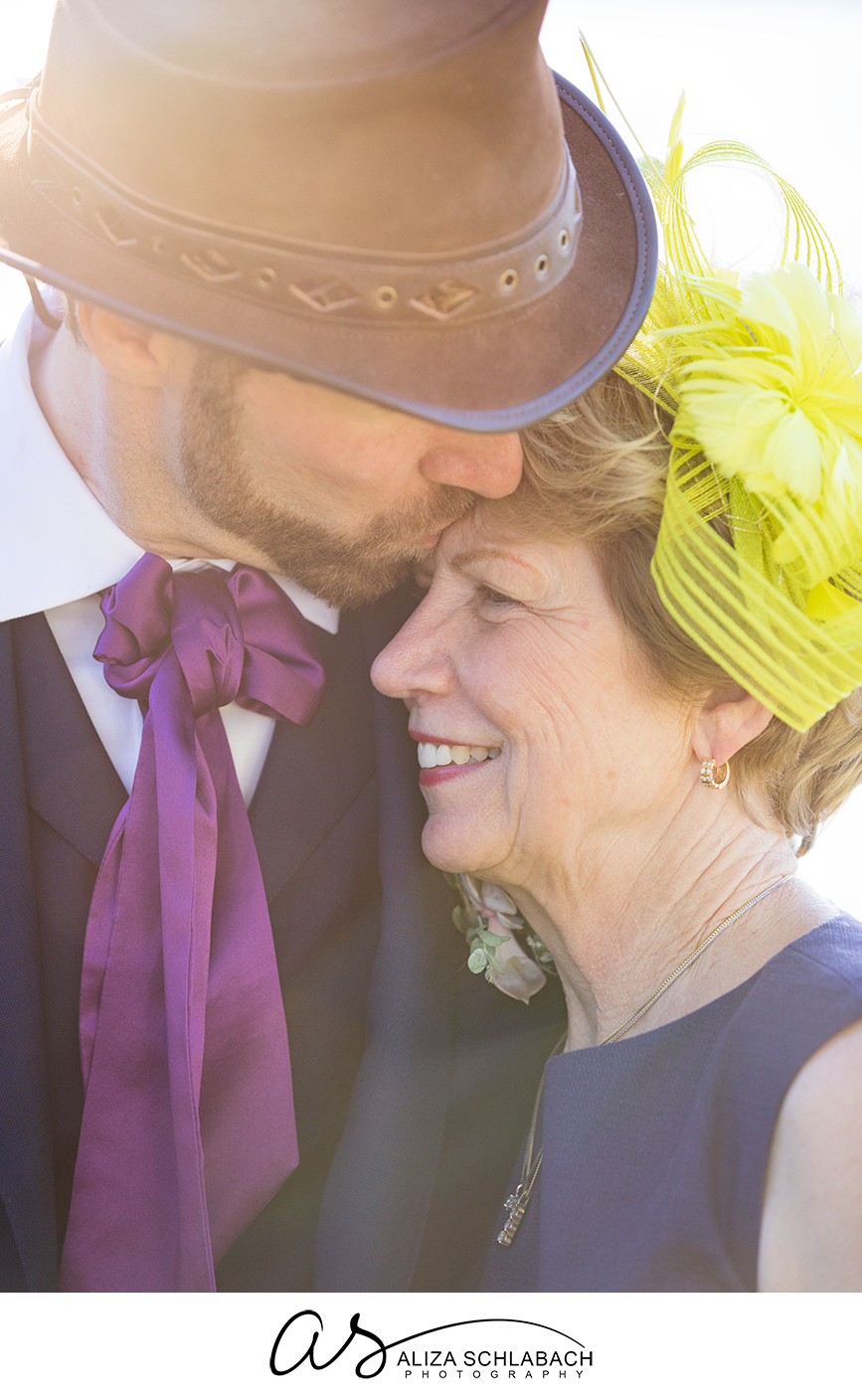 Backlit photograph of groom in hat kissing his mother's forehead