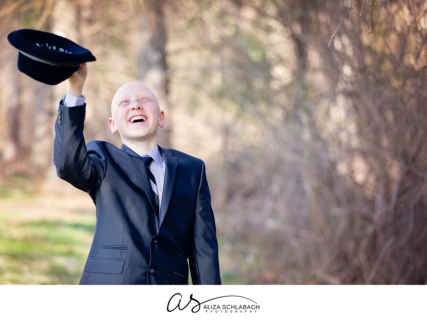 Outdoor portrait of boy in a suit with alopecia universalis smiling and waving his hat