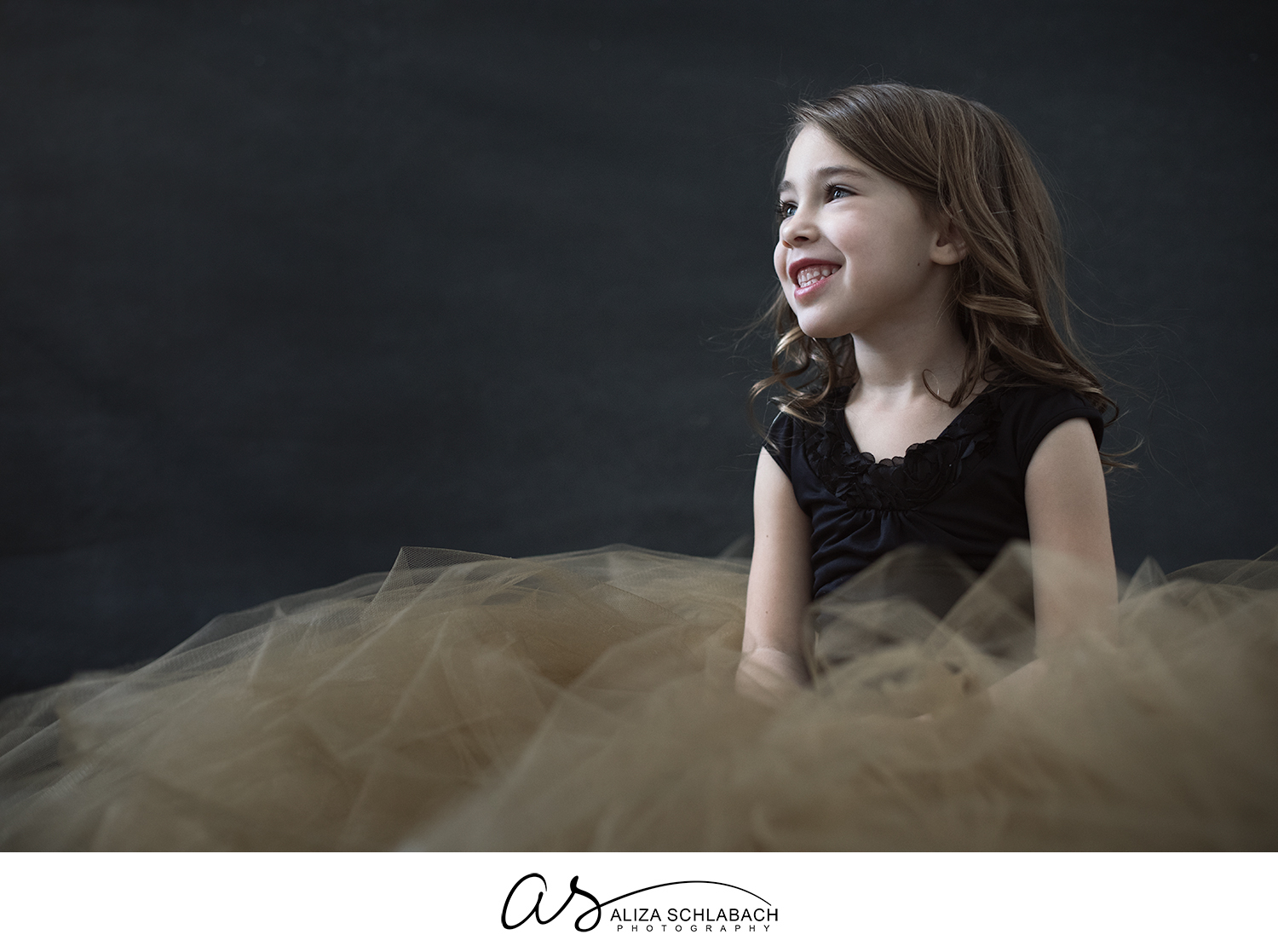Portrait of a smiling little girl sitting in a gold tulle skirt