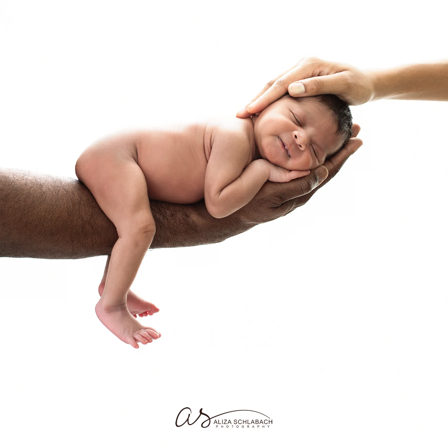 Backlit photo of a naked black newborn baby being cradled between her parents' hands