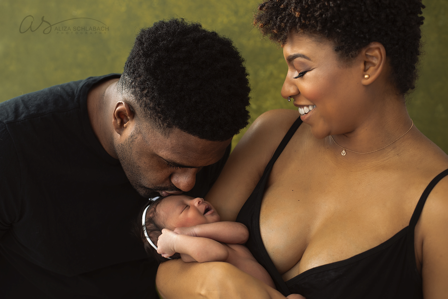 Photo of black mom holding newborn baby while dad kisses her