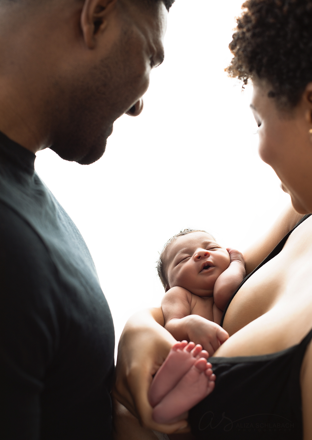 Backlit photo of black mom and dad holding their newborn baby