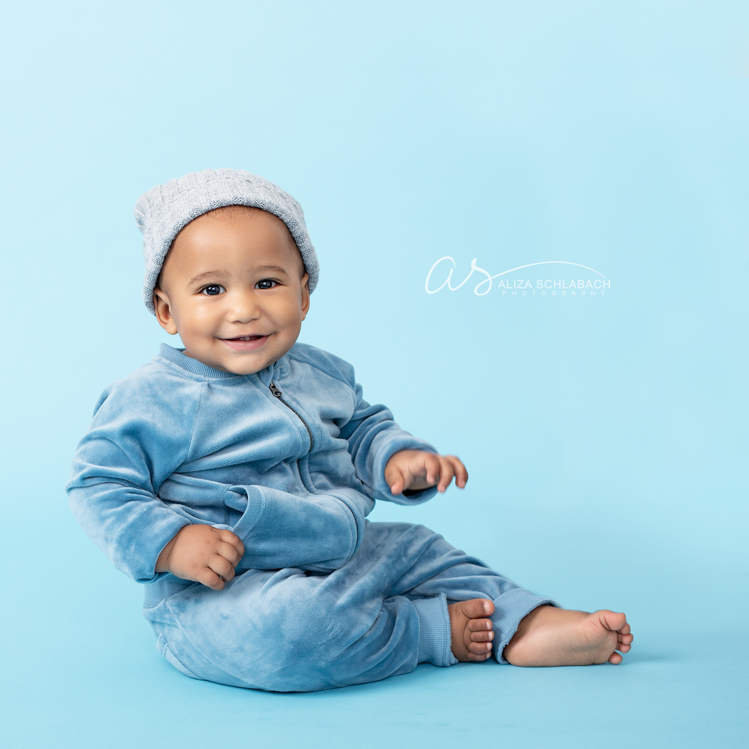 Adorable black baby sitting up in a blue track suit and hat