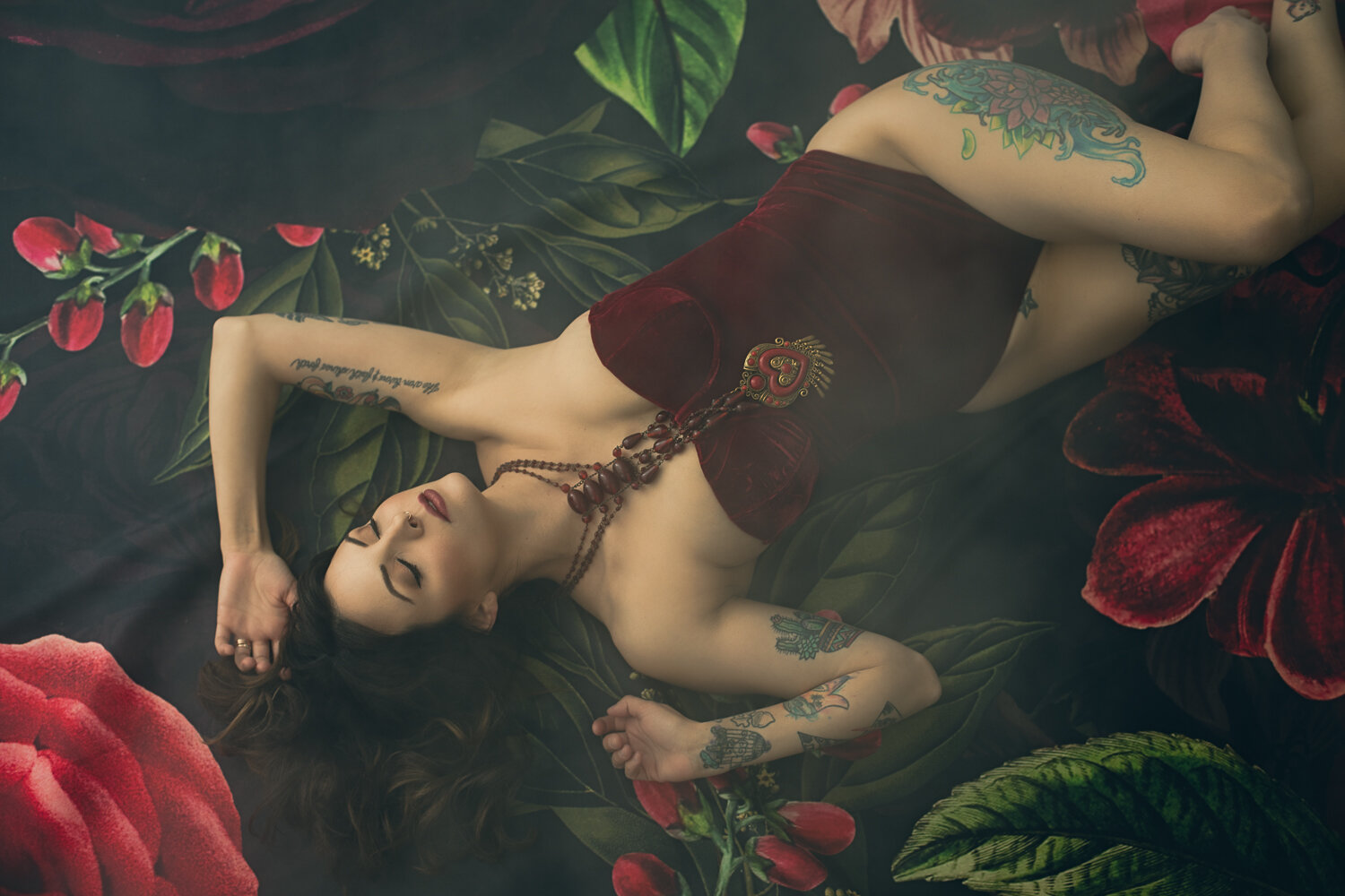 Photo of a beautiful tattooed woman in a red velvet bodysuit on a red and green floral drop