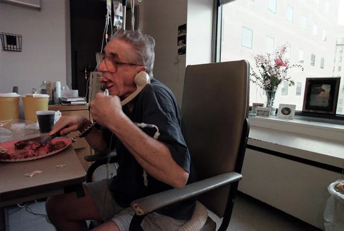 Flying in the face of hospital rules, John grills himself a steak in his room while talking to a fishing buddy.