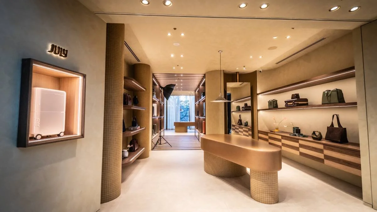 Interior of a modern retail store with shelves displaying handbags, accessories, and cameras, a curved display counter, and soft lighting.