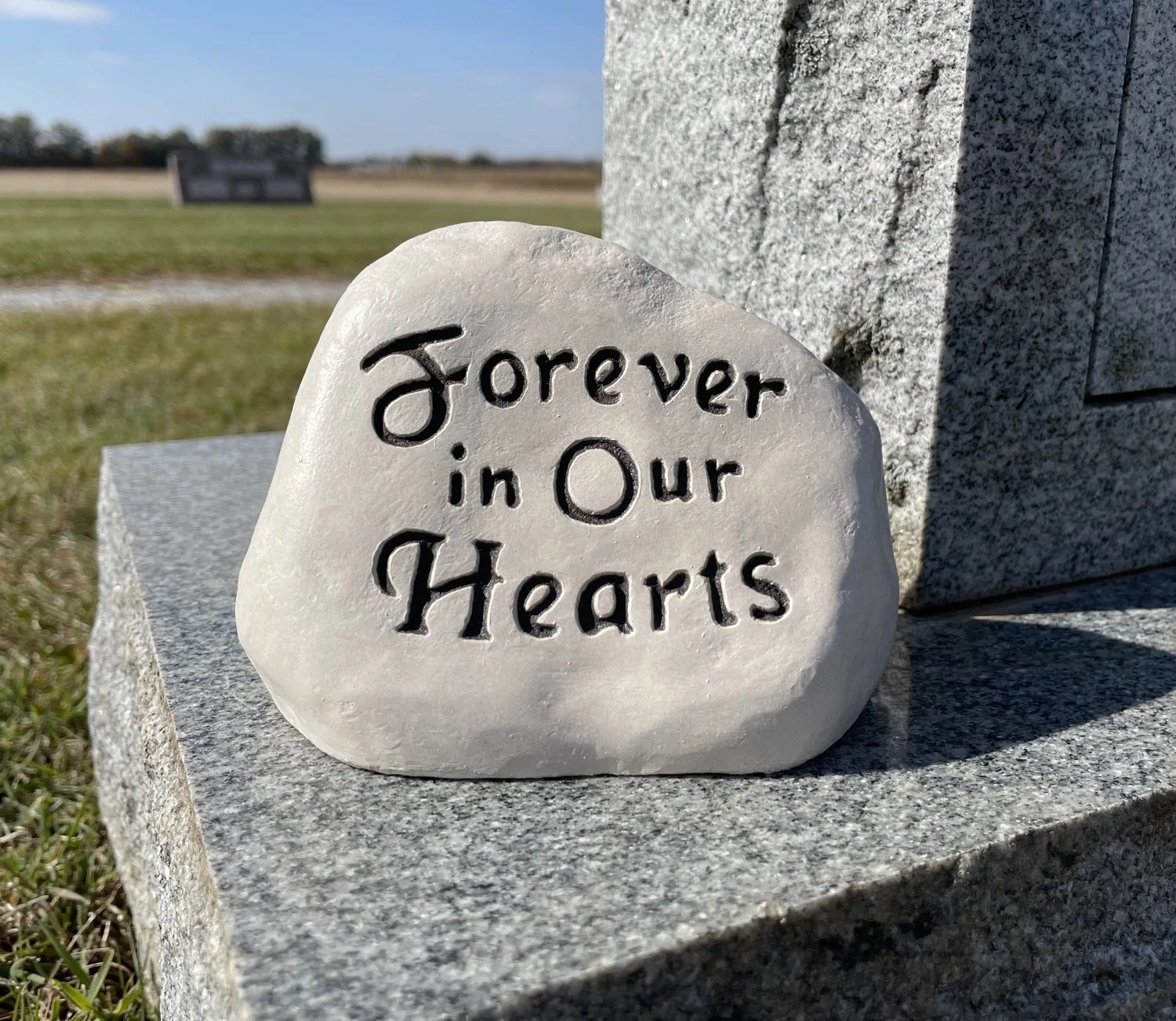Small engraved memorial rock placed as a grave marker tribute next to a cemetery headstone for a loved one.