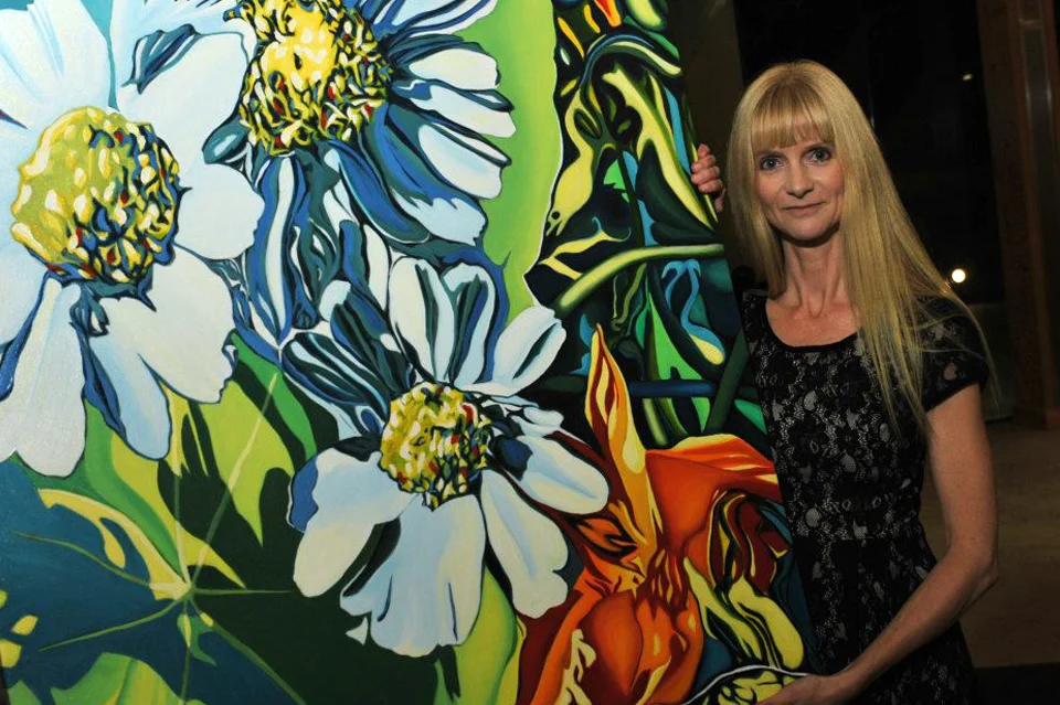 Grant recipient Anne Gudrun stands next to her painting "Daisies" at the "Tribute to the Arts" event.
