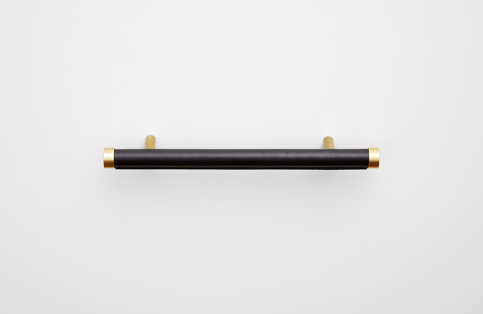 Brass handle wrapped in black leather against a white wall 