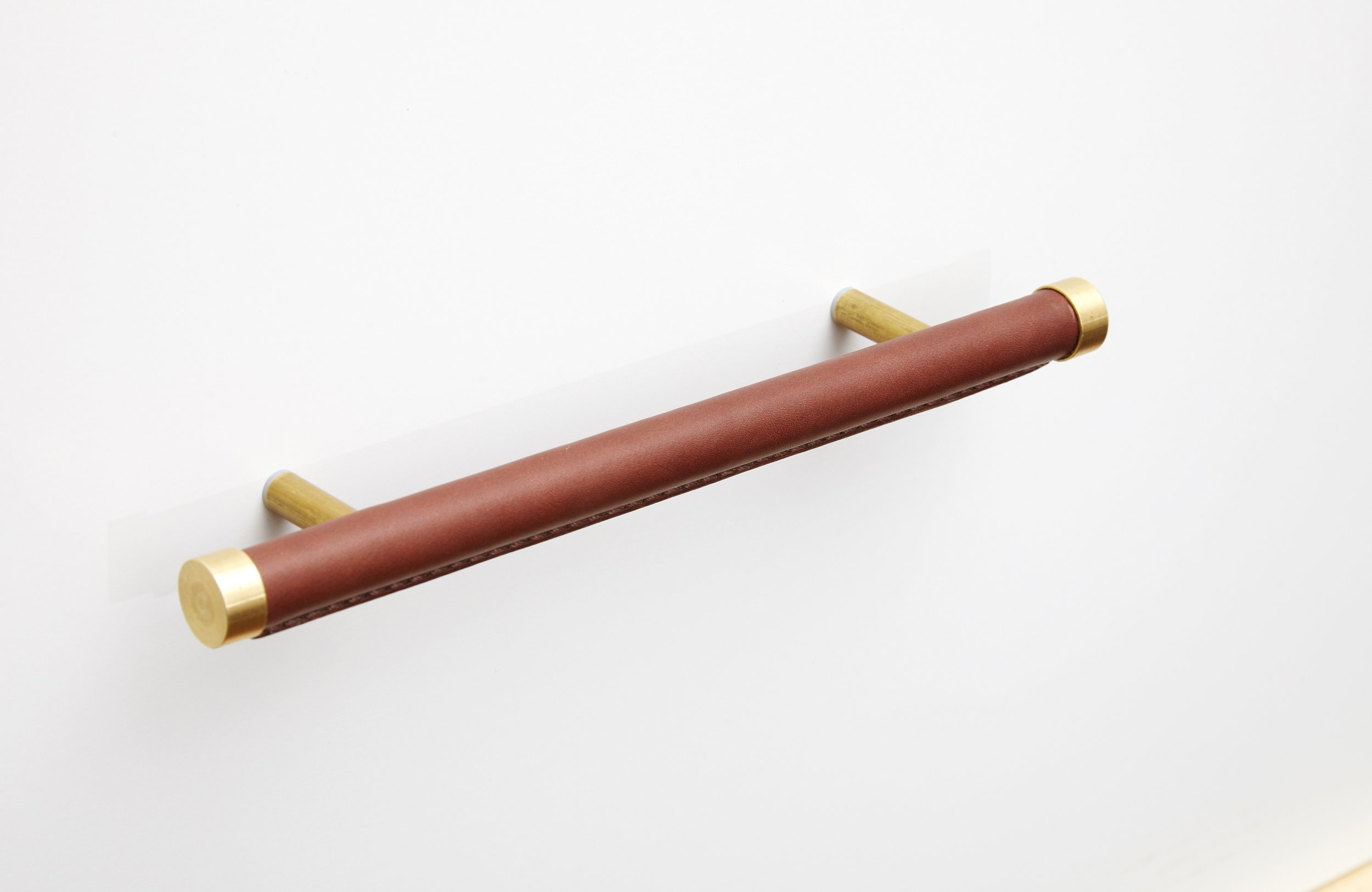 Brass handle wrapped in brown leather against a white wall 