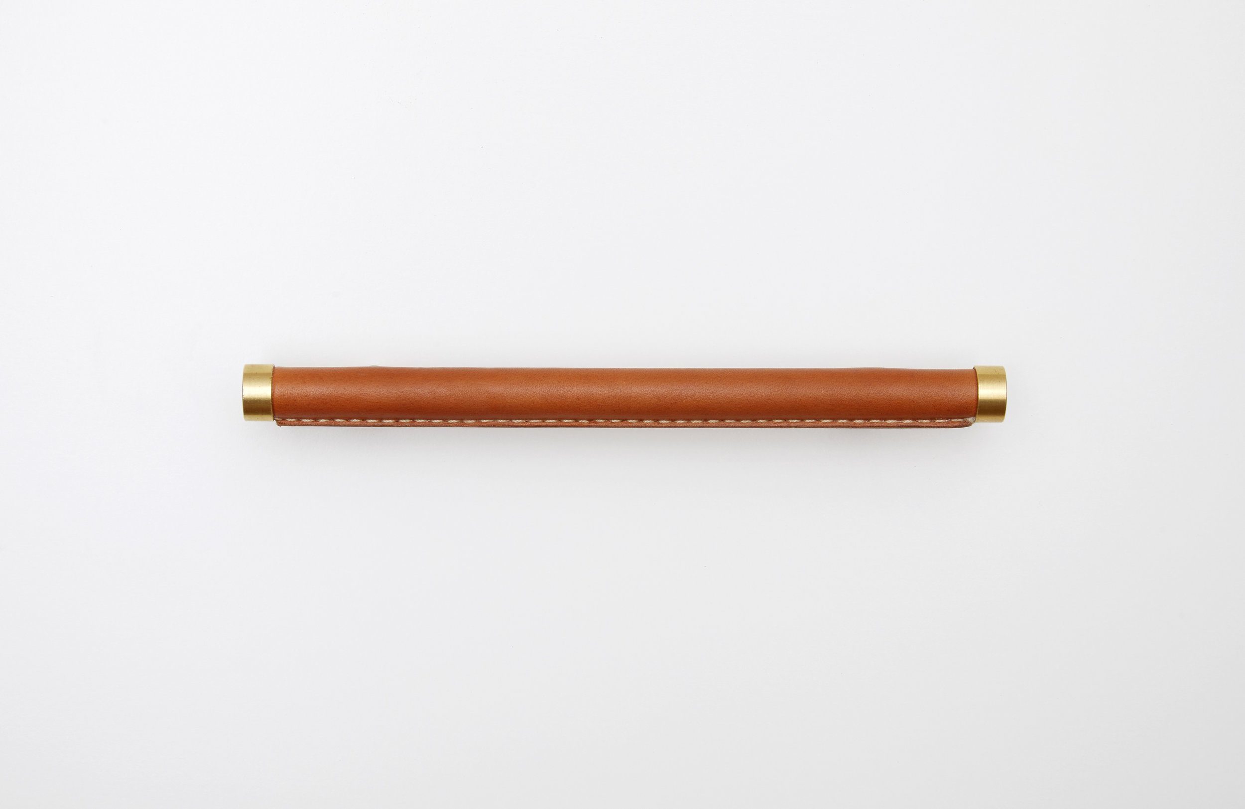 Brass handle wrapped in natural skirting leather against a white wall 