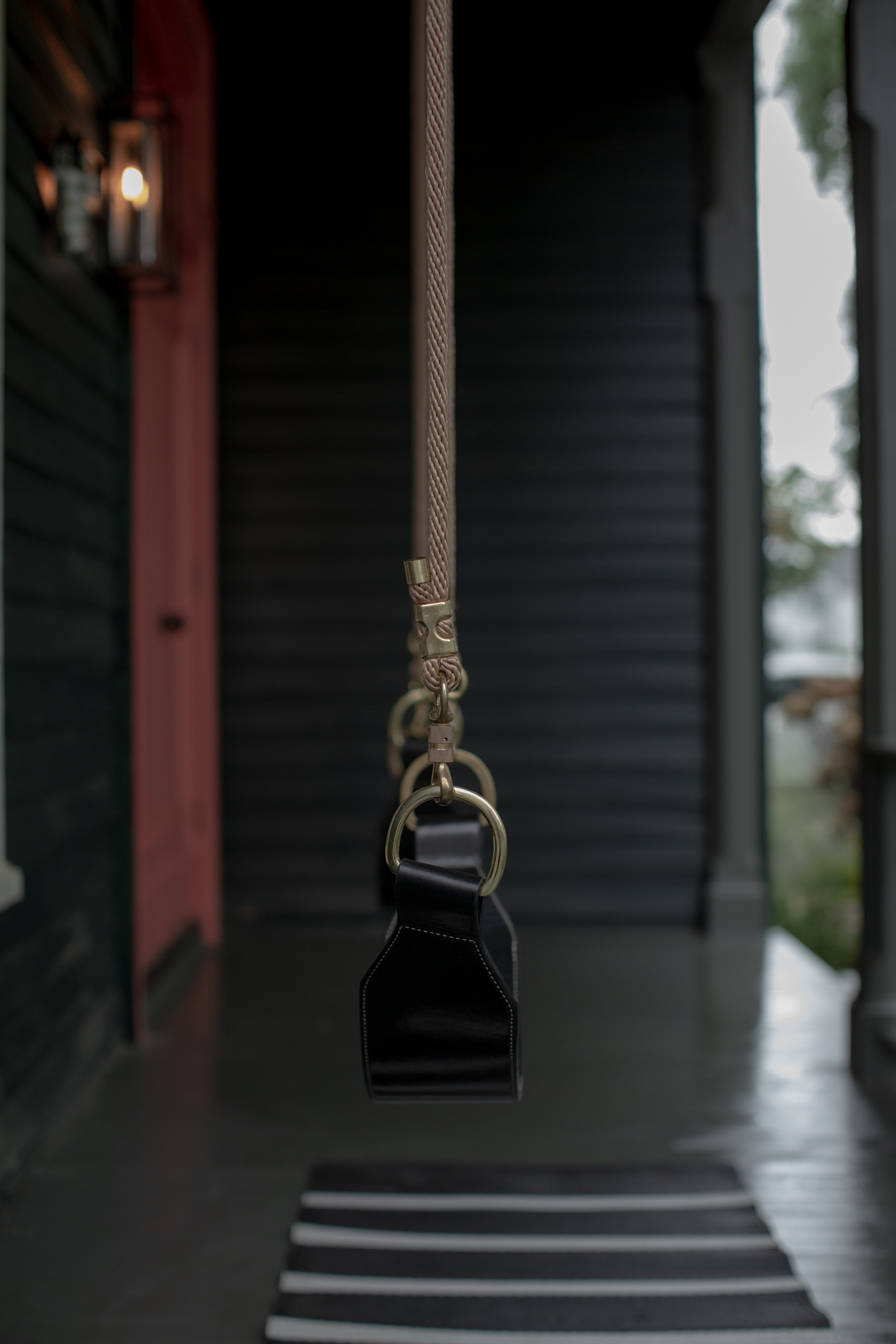 Side view of black leather swing with brass hardware shown on porch