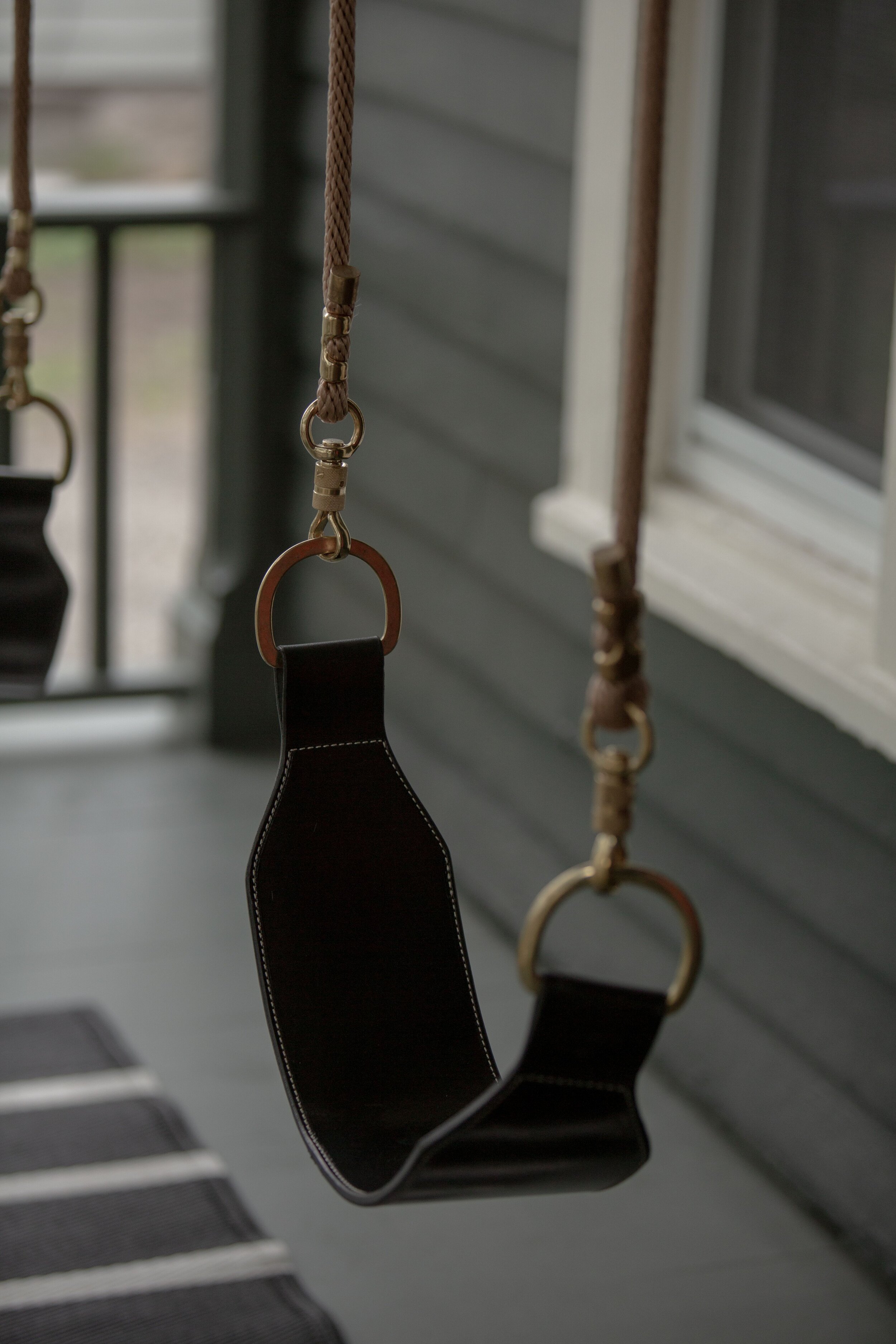 Black leather swing with brass hardware and braided polyester rope shown on porch