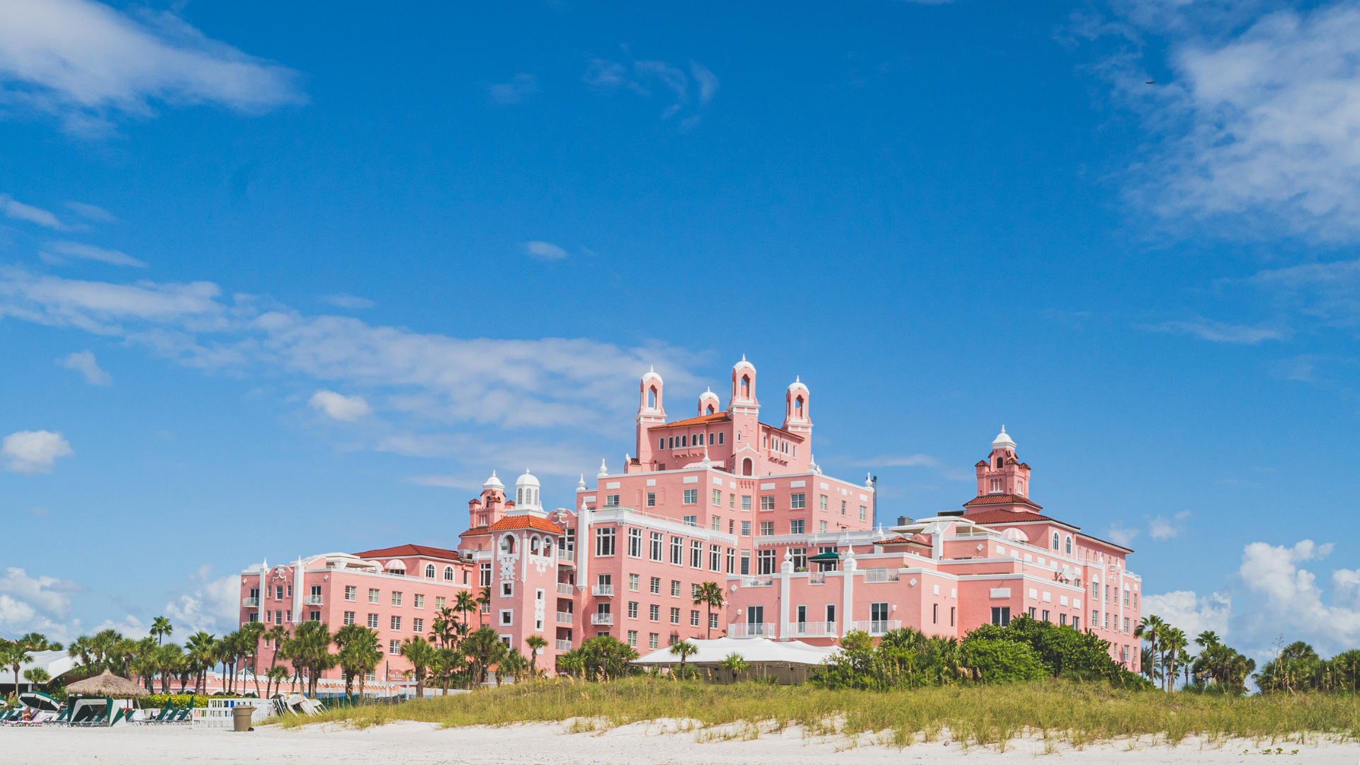 Pink castle-like hotel on a beach with blue sky and white clouds