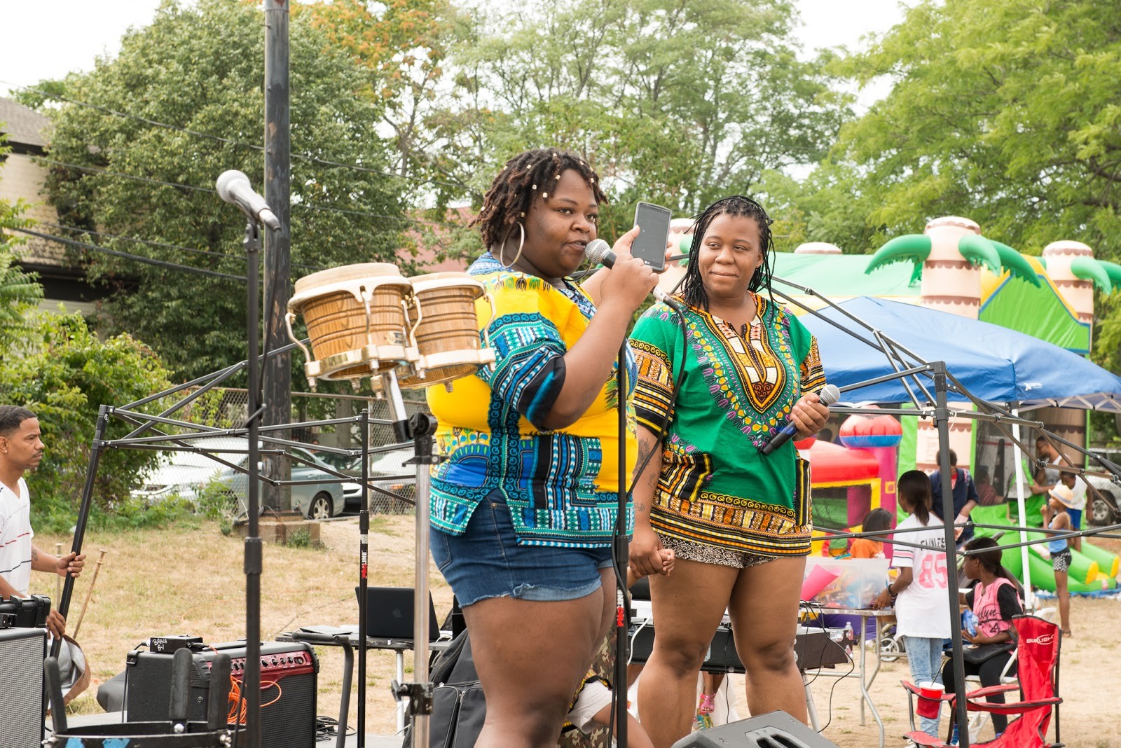 Jaimorry Carter and Ava Mootrey perform at DSNI’s 28th Annual Multicultural Festival. Image shows Jaimorry, in a yellow and blue tunic, speaking into a microphone and Ava, in a green and orange tunic, holding a microphone, at Mary Hannon Park in Dorchester. Photography by Mark Fusco.