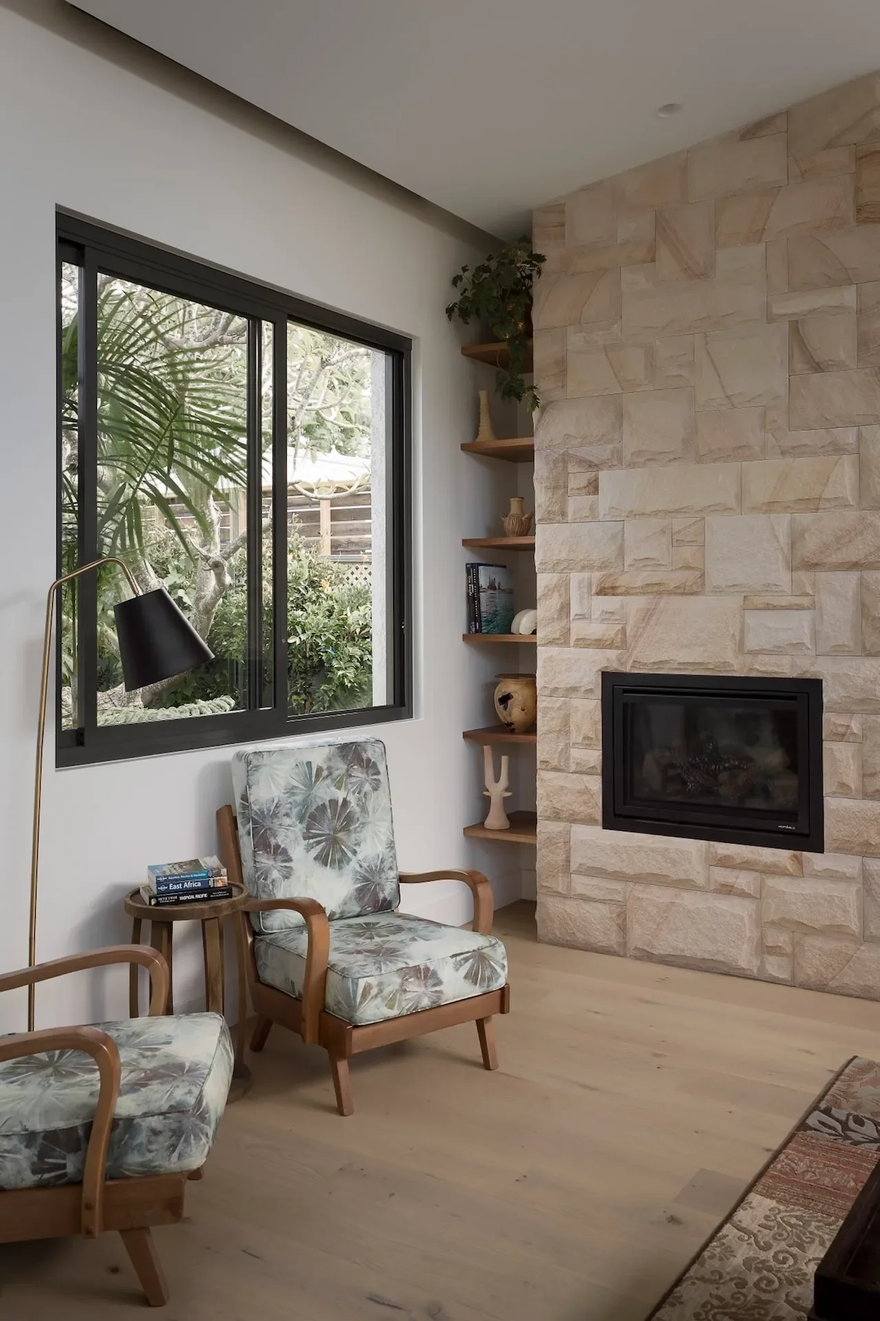 Living room with stone fireplace, timber shelving and garden outlook in a family home renovation.