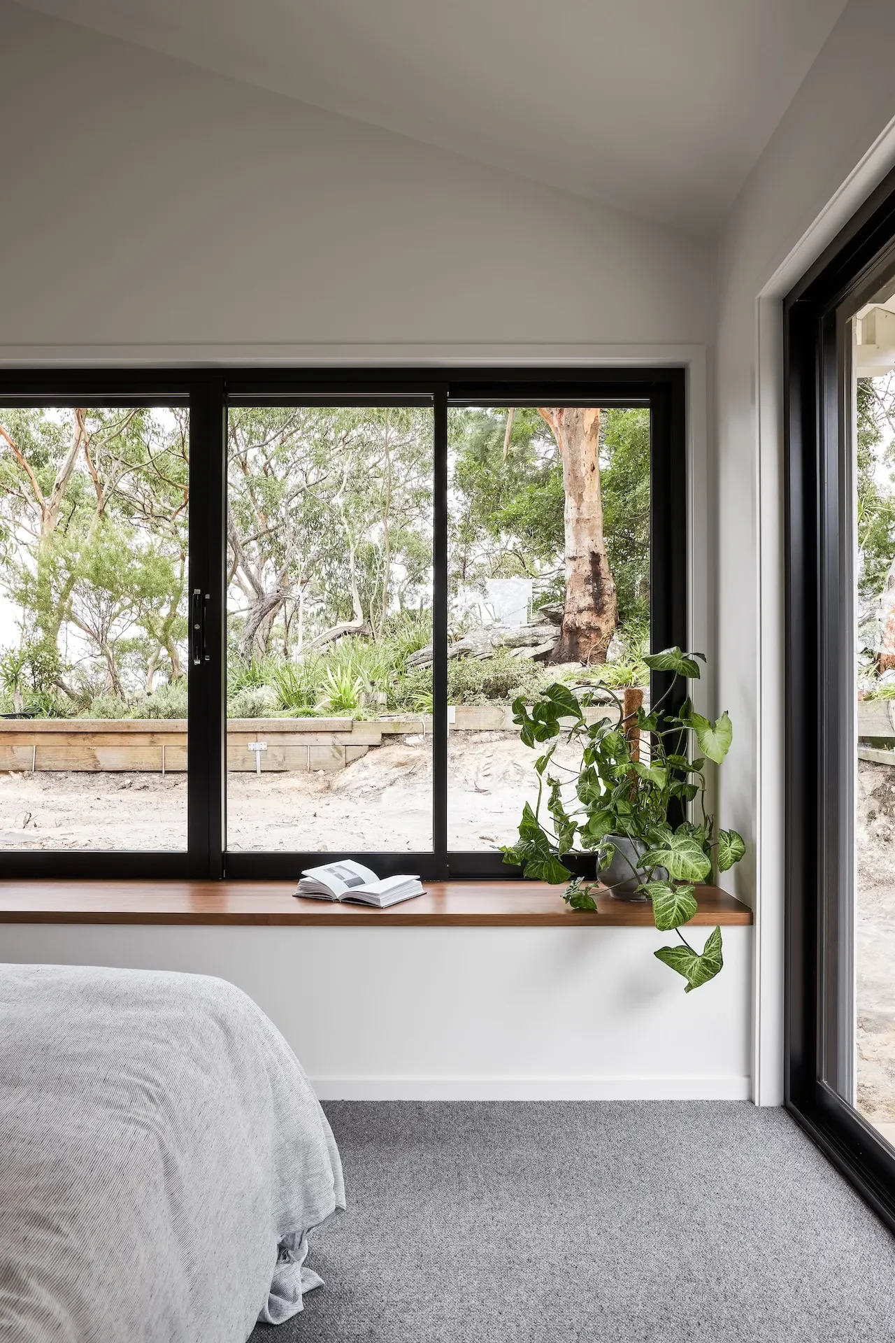 Bedroom with large window framing bushland views, designed to maximise natural light and connection to nature.