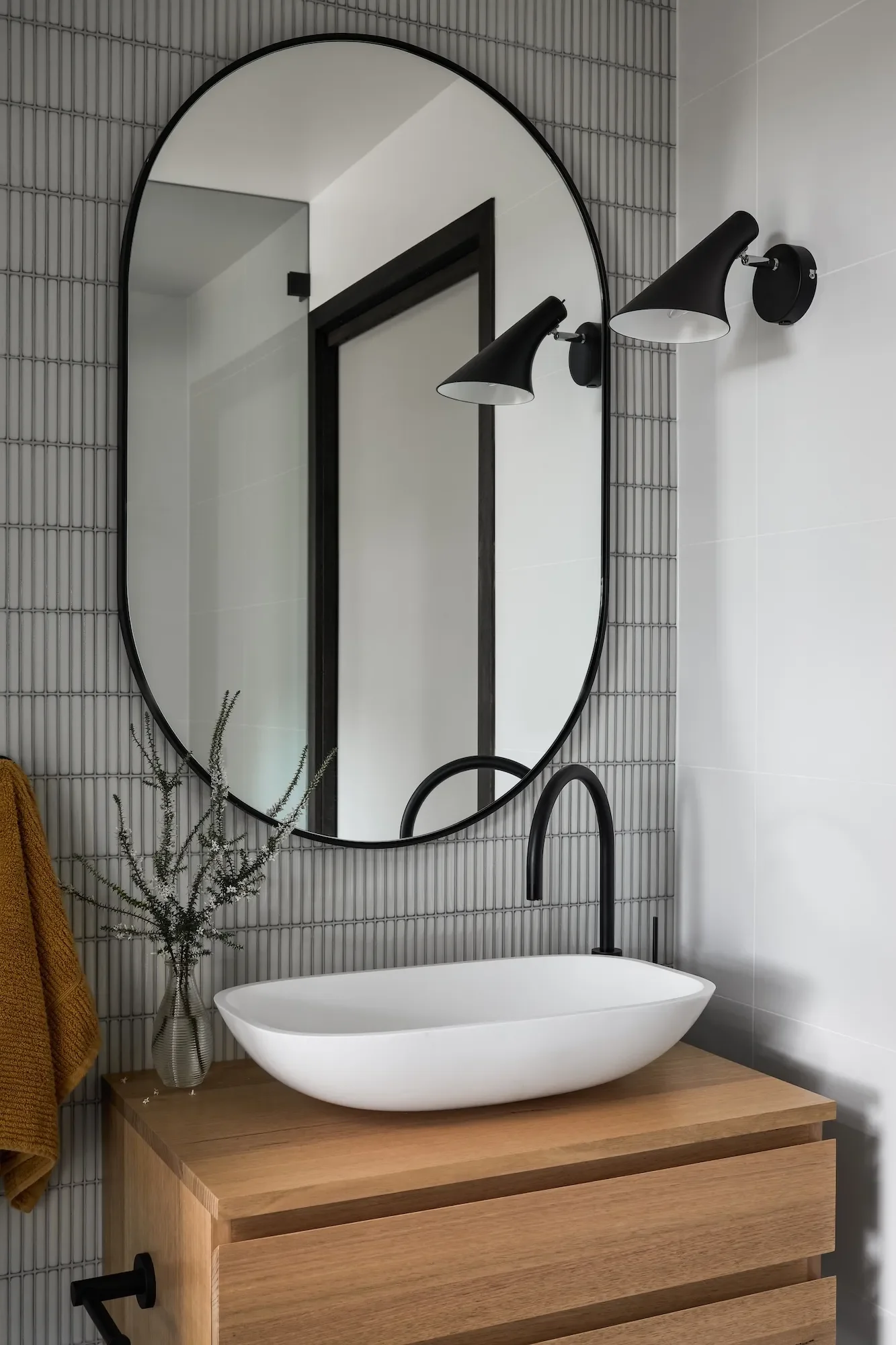 Bathroom with curved mirror, textured tiles and refined black fixtures.