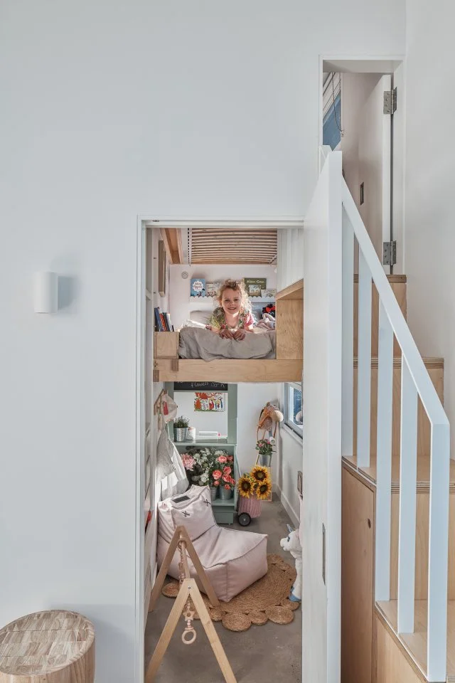 looking through doorway at a small kids room with a loft, toys, small furniture and a smiling child
