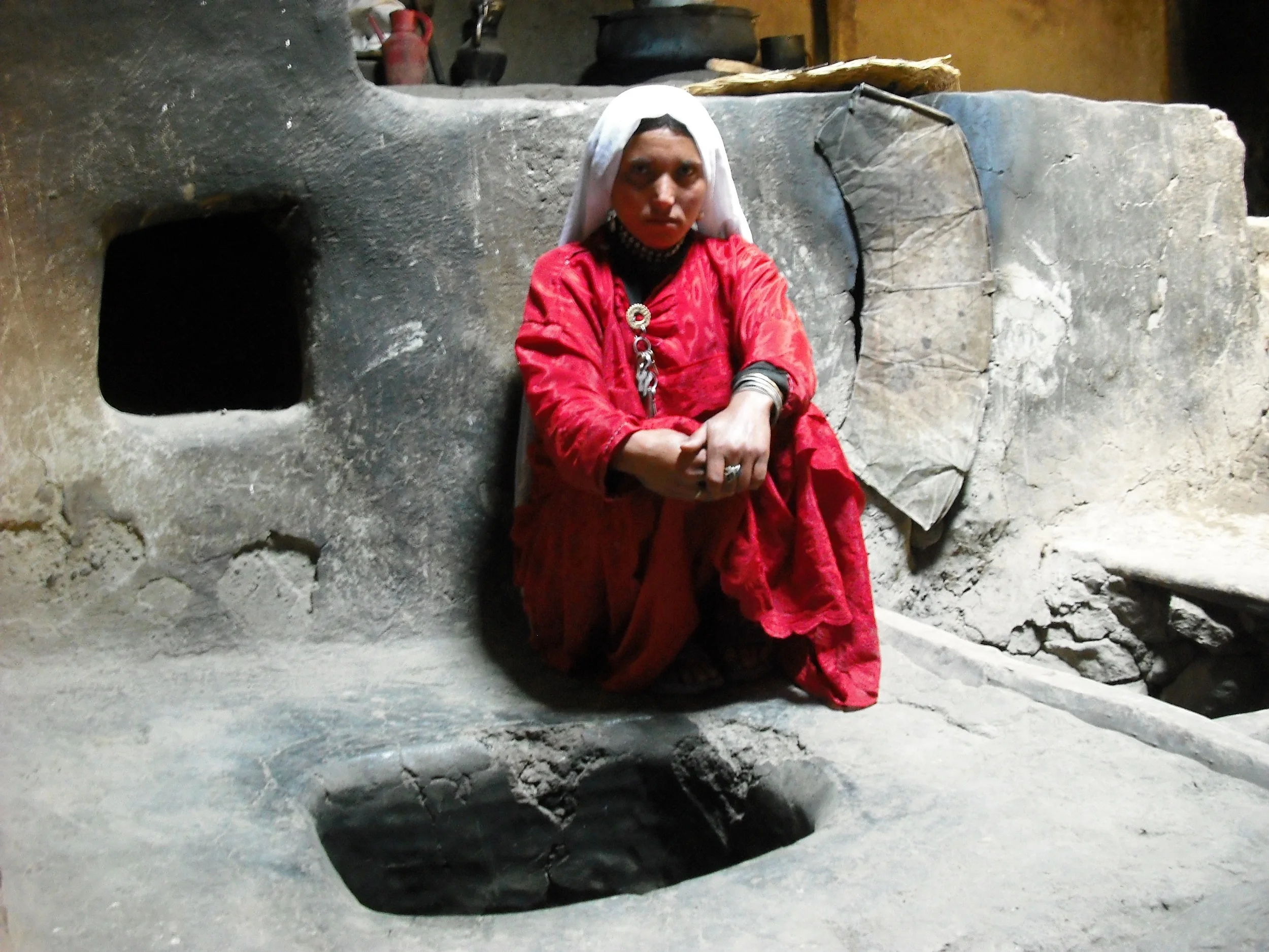 This Afghan Ismaili woman is sitting beside&nbsp;a traditional hearth. &nbsp;Its&nbsp; fire would both warm the house and be used to cook food.&nbsp; Cooking over a fire is difficult and can be dangerous.&nbsp; A number of development initiatives in…