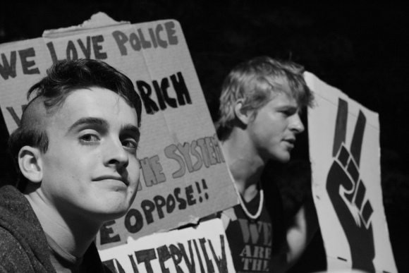 8 October 2011 Two protesters welcome passersby to ask them questions about the meaning and goals of the Occupy Wall Street movement. “We love police. We love rich people. It’s the system we oppose!!” says their sign.