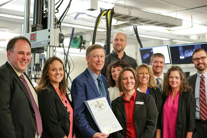 ADAPT team members celebrate the Governor's proclamation, naming October Colorado Manufacturing Month. Left to right: Aaron Stebner, Katie Woslager, Governor John Hickenlooper, Brandan Kappes, Mickele Bragg, Sumer Sorensen-Bain, Heidi Hostetter, Craig Brice, Alicia Svaldi and Douglas Van Bossuyt.