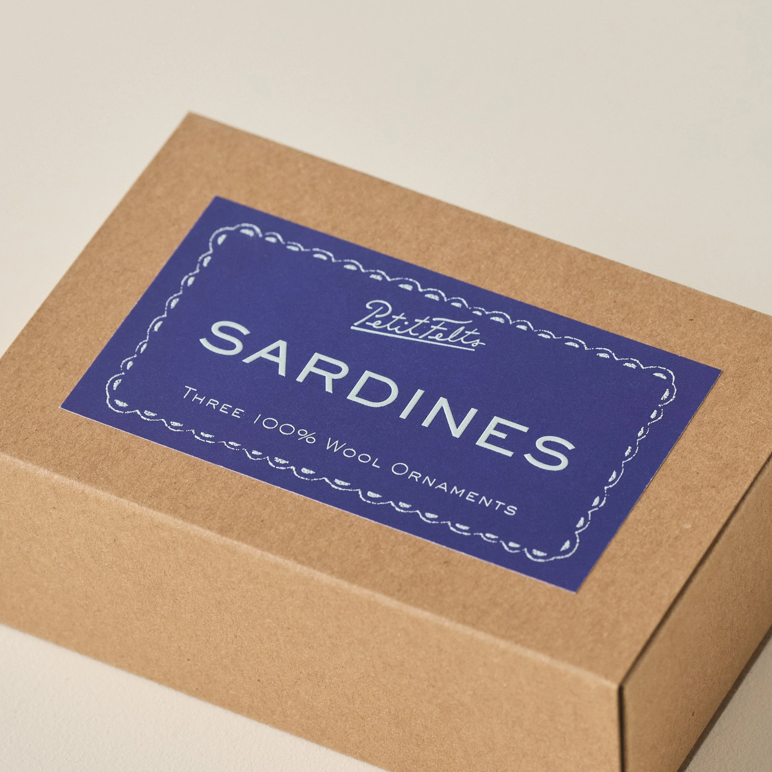 Detail of the PetitFelts Sardines Ornament Box detail with blue background label and light blue raised ink text