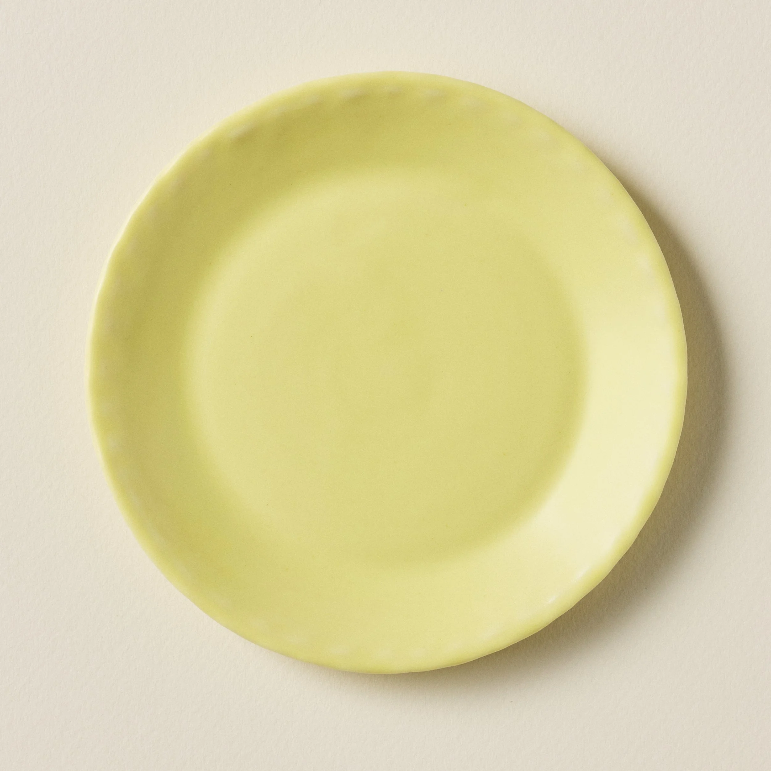 Overhead view of the PetitFelts Custard yellow ceramic plate, handmade with a scalloped edge