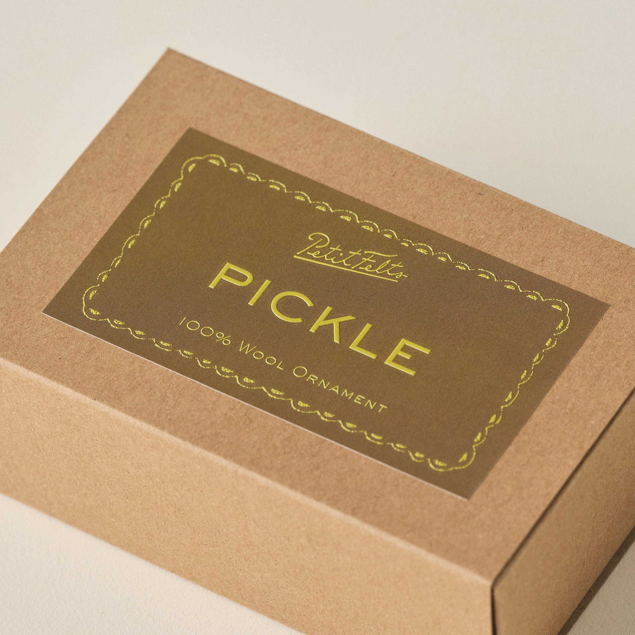 Detail of the PetitFelts Christmas Pickle ornament box with olive background and chartreuse raised ink