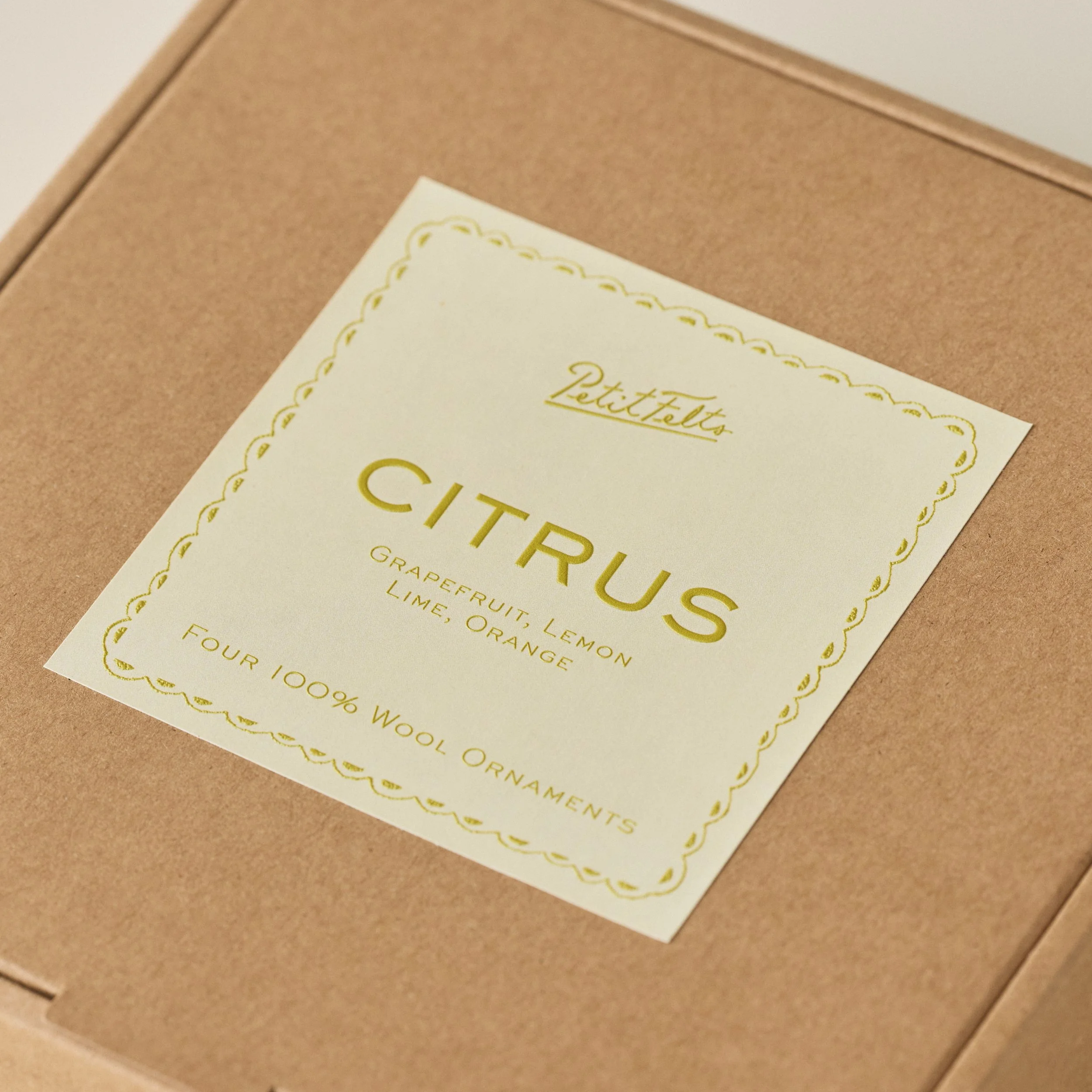 Detail of label on PetitFelts citrus ornament set with butter yellow background and raised chartreuse ink