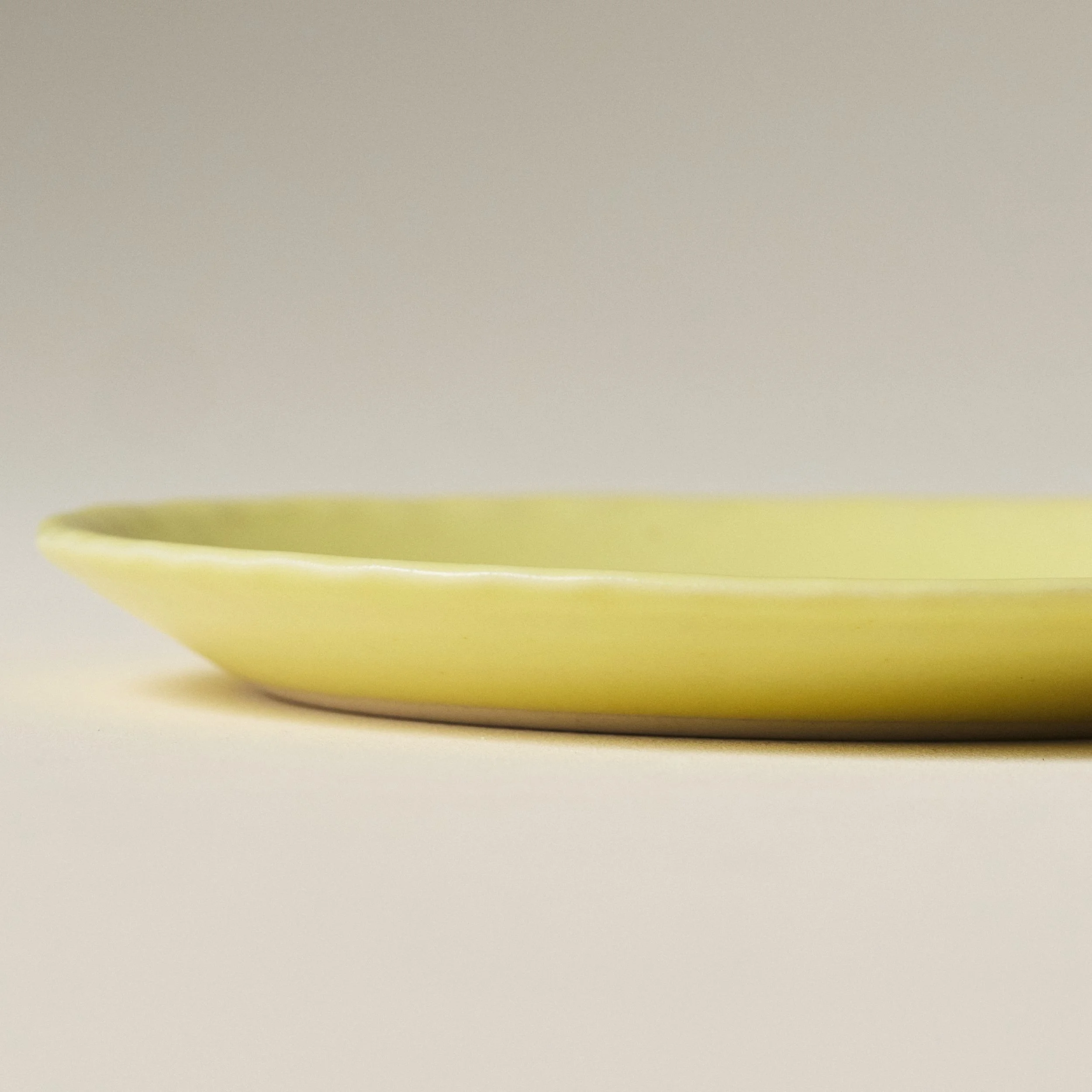 Side view of the PetitFelts Custard yellow ceramic plate showing its fluted rim