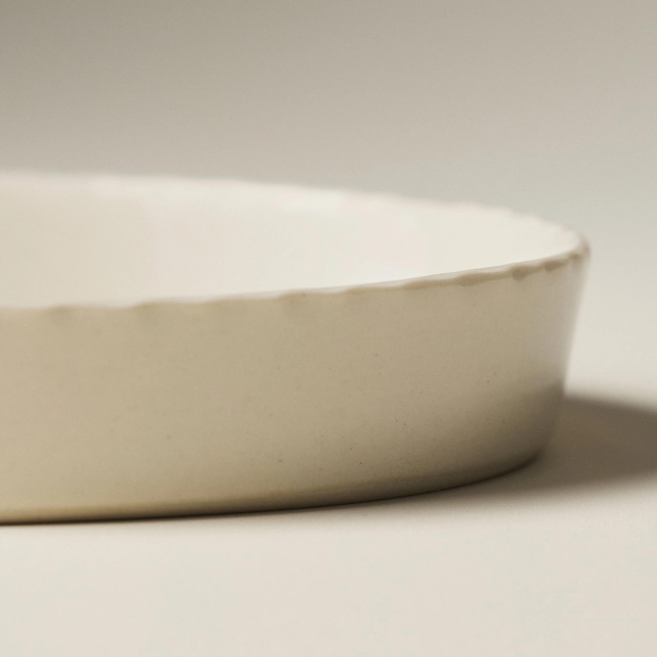 Side view of the PetitFelts Natural ceramic platter showing its scalloped rim