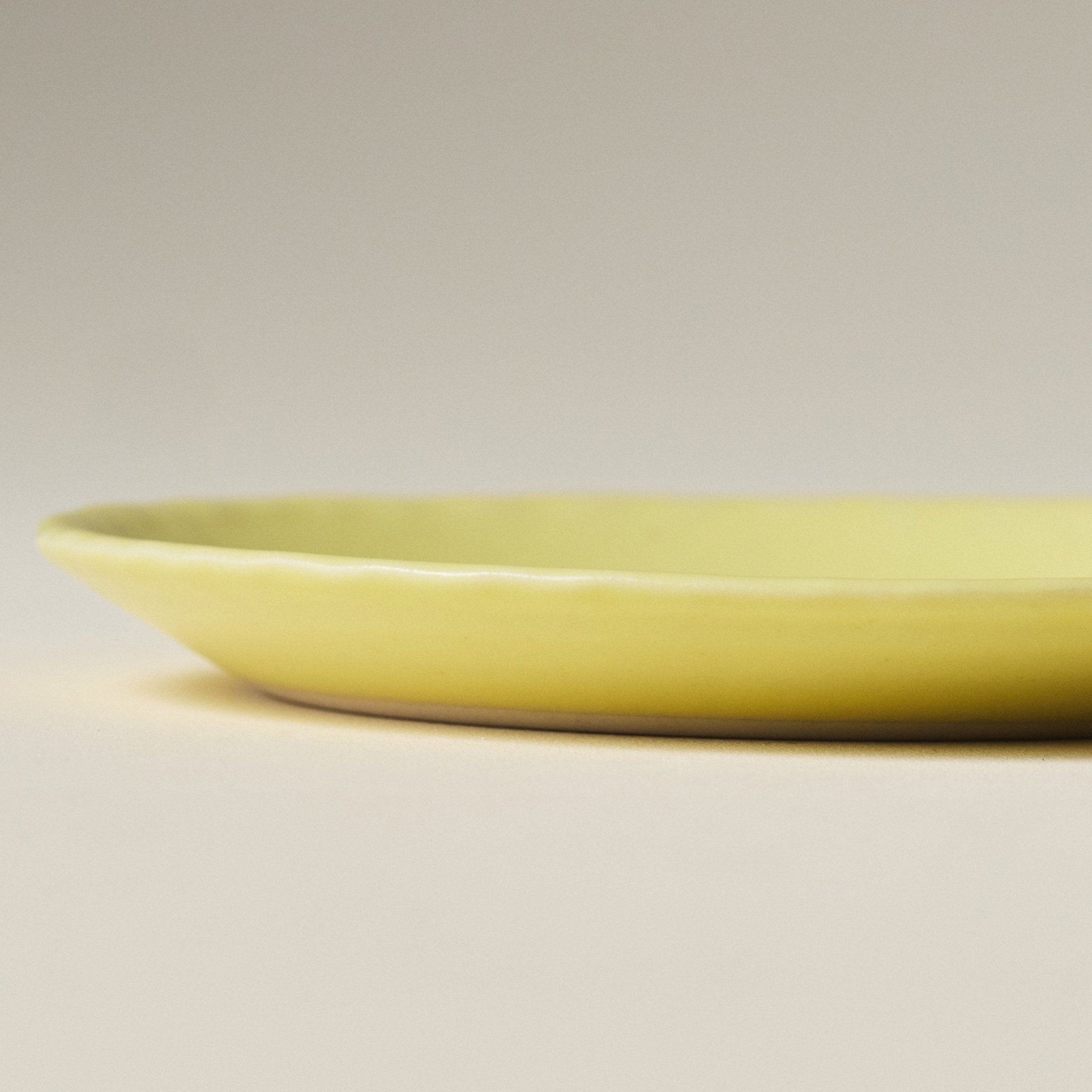 Side view of the PetitFelts Custard yellow ceramic plate showing its fluted rim