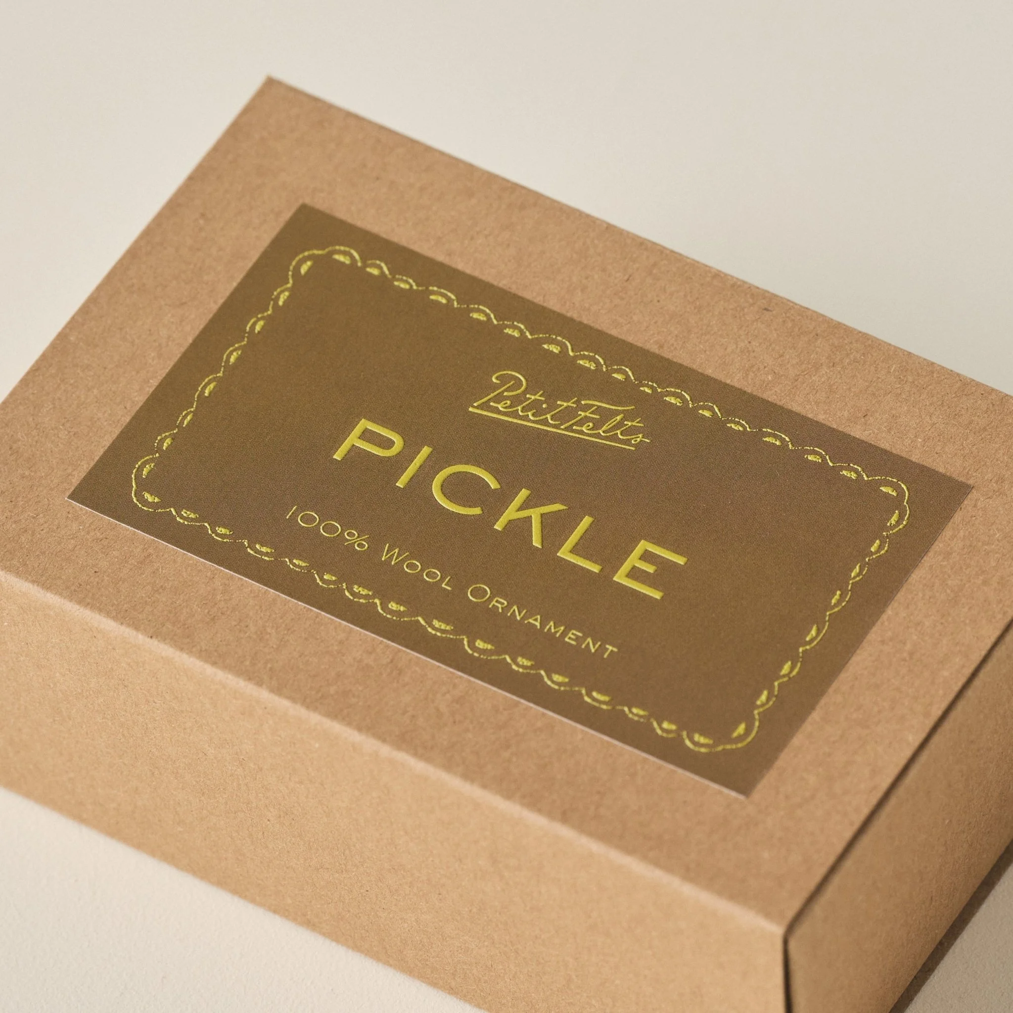 Detail of the PetitFelts Christmas Pickle ornament box with olive background and chartreuse raised ink