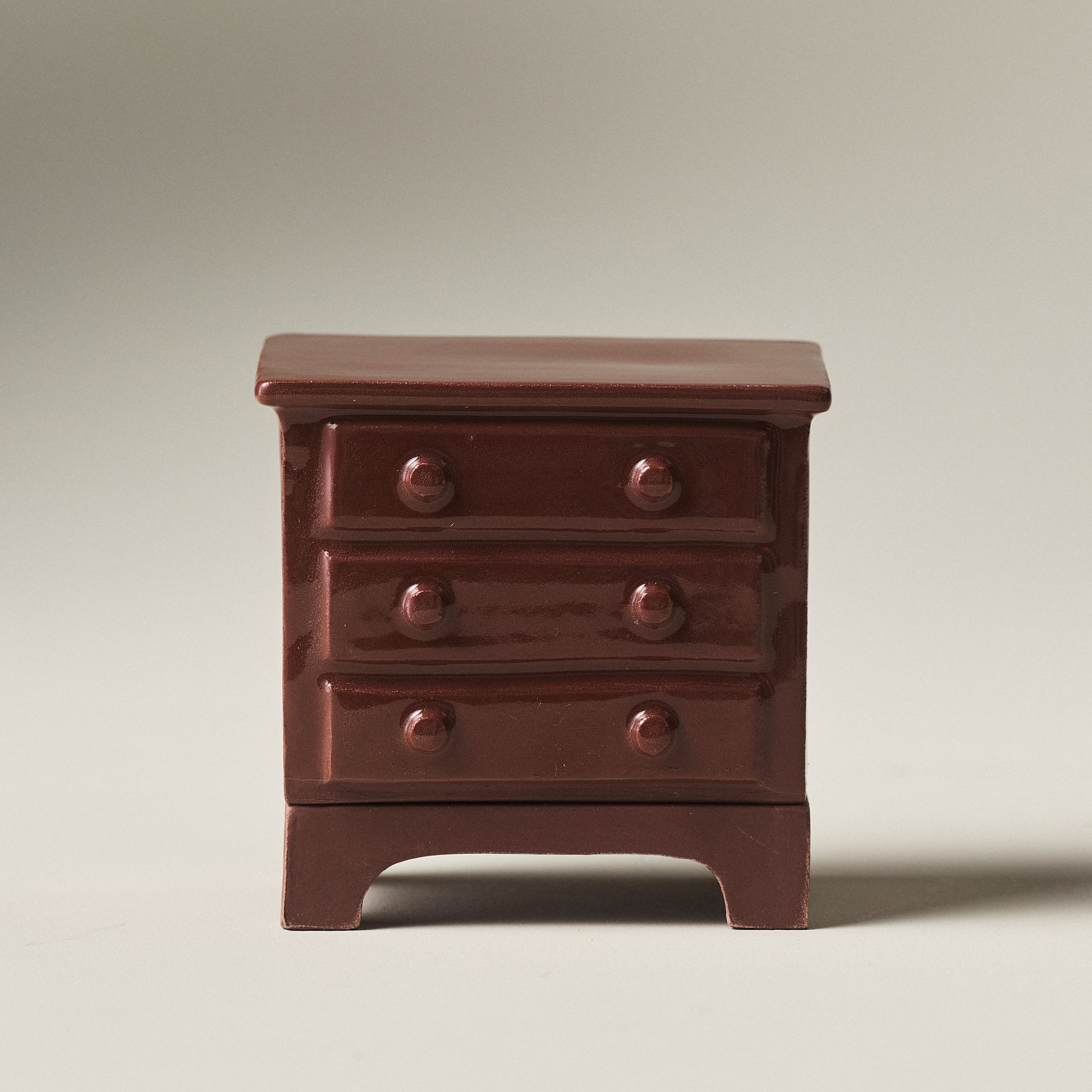 Front view of a hand-glazed porcelain dresser match striker with three drawers
