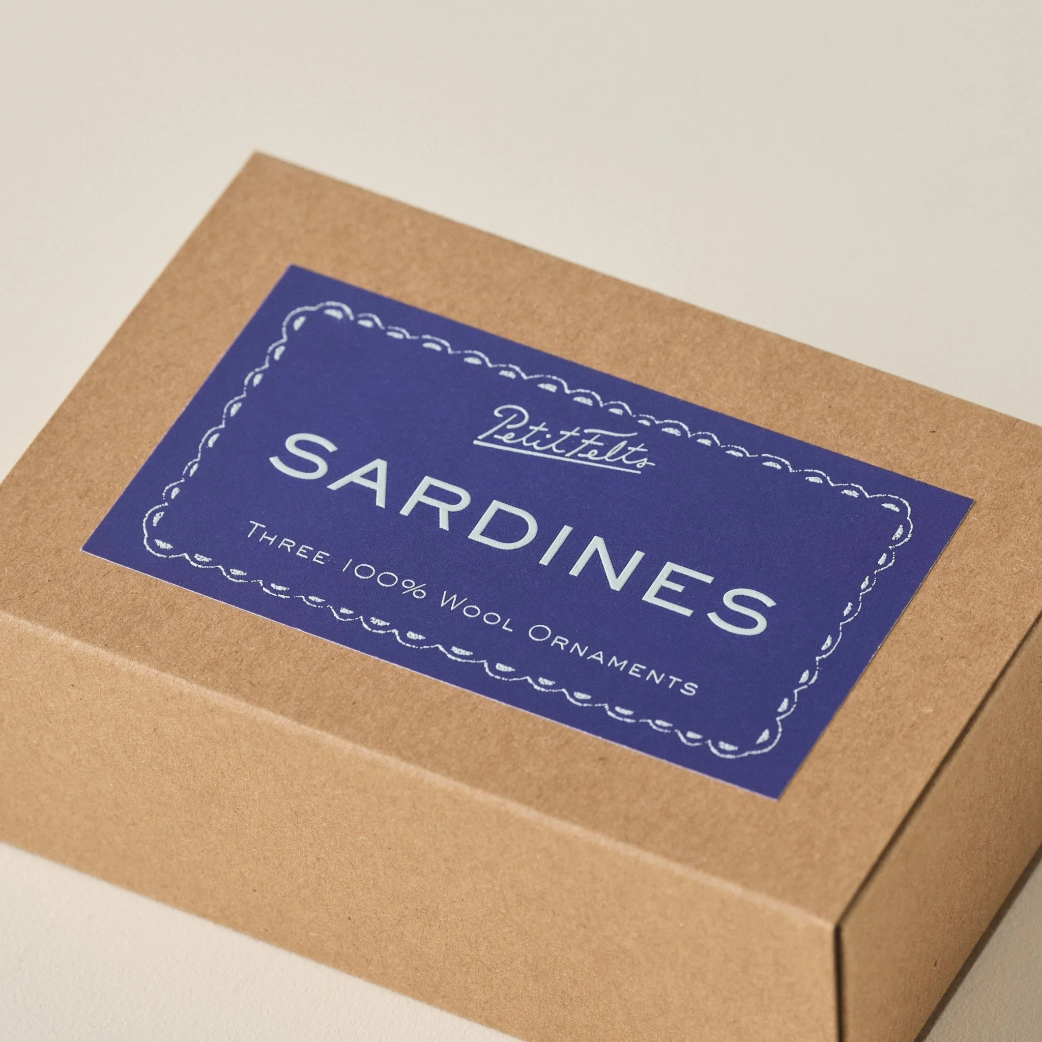 Detail of the PetitFelts Sardines Ornament Box detail with blue background label and light blue raised ink text