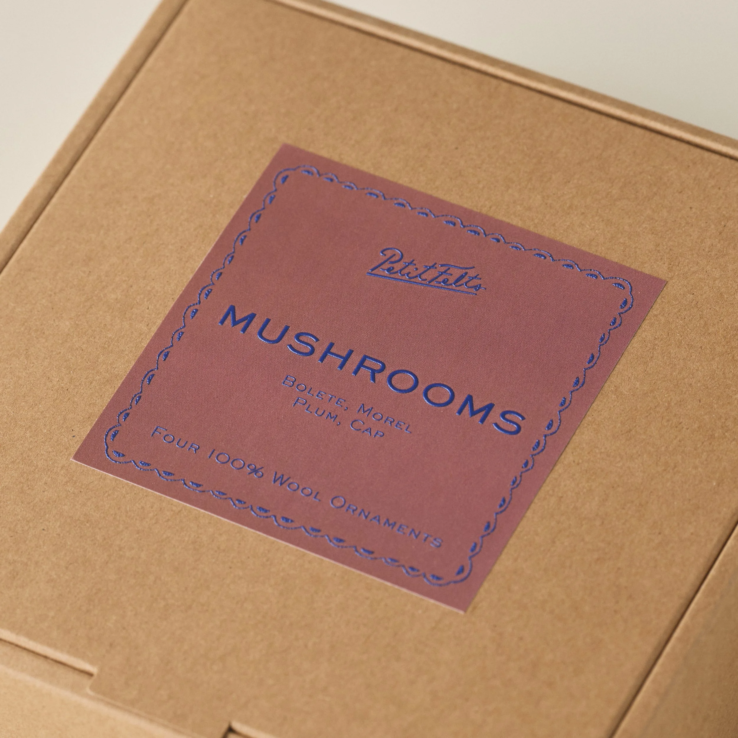 Detail of the mauve PetitFelts Mushroom Ornament set box label with blue raised ink