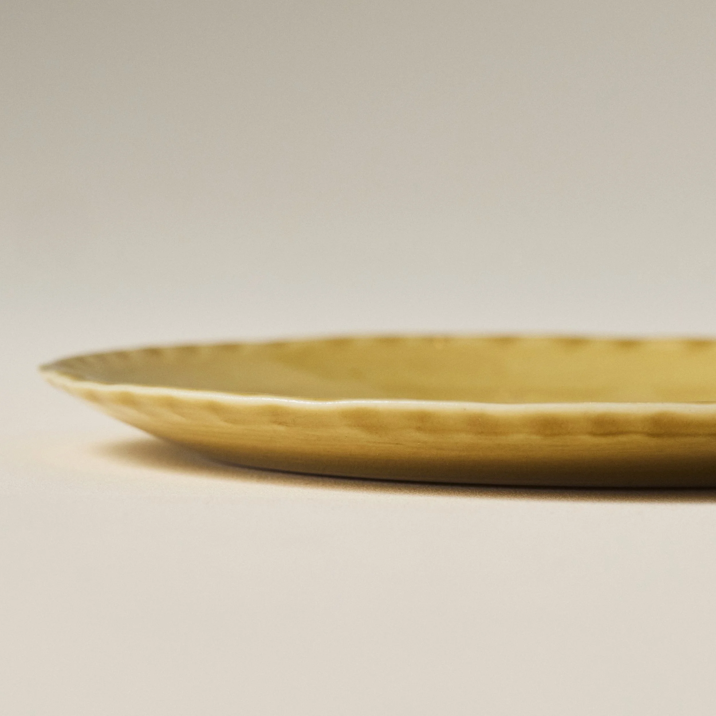 Side view of the PetitFelts Fennel yellowish-green  ceramic plate showing its fluted rim