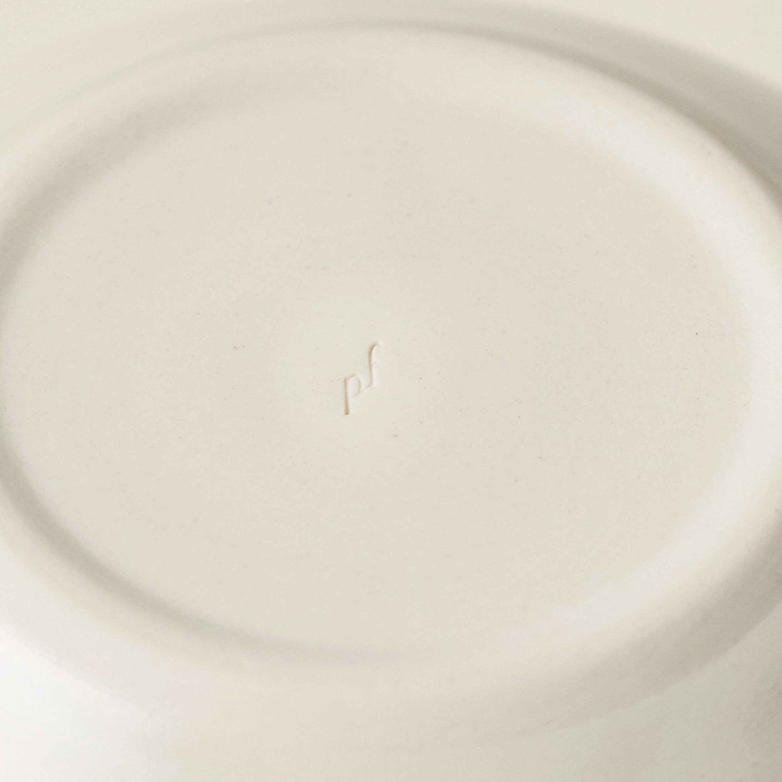 Underside detail of the PetitFelts Natural ceramic dinner bowl showing the maker's mark