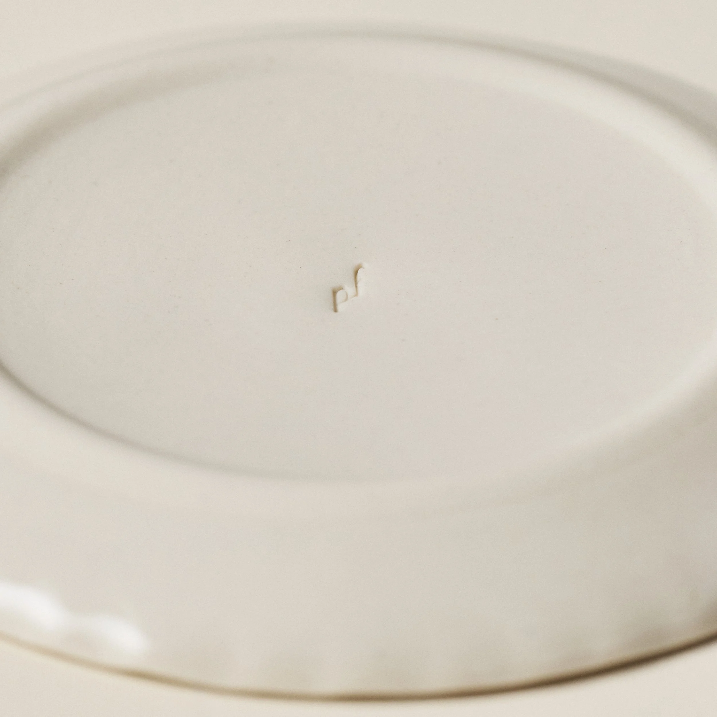 Close-up detail of the PetitFelts Natural small ceramic plate showing the maker's mark