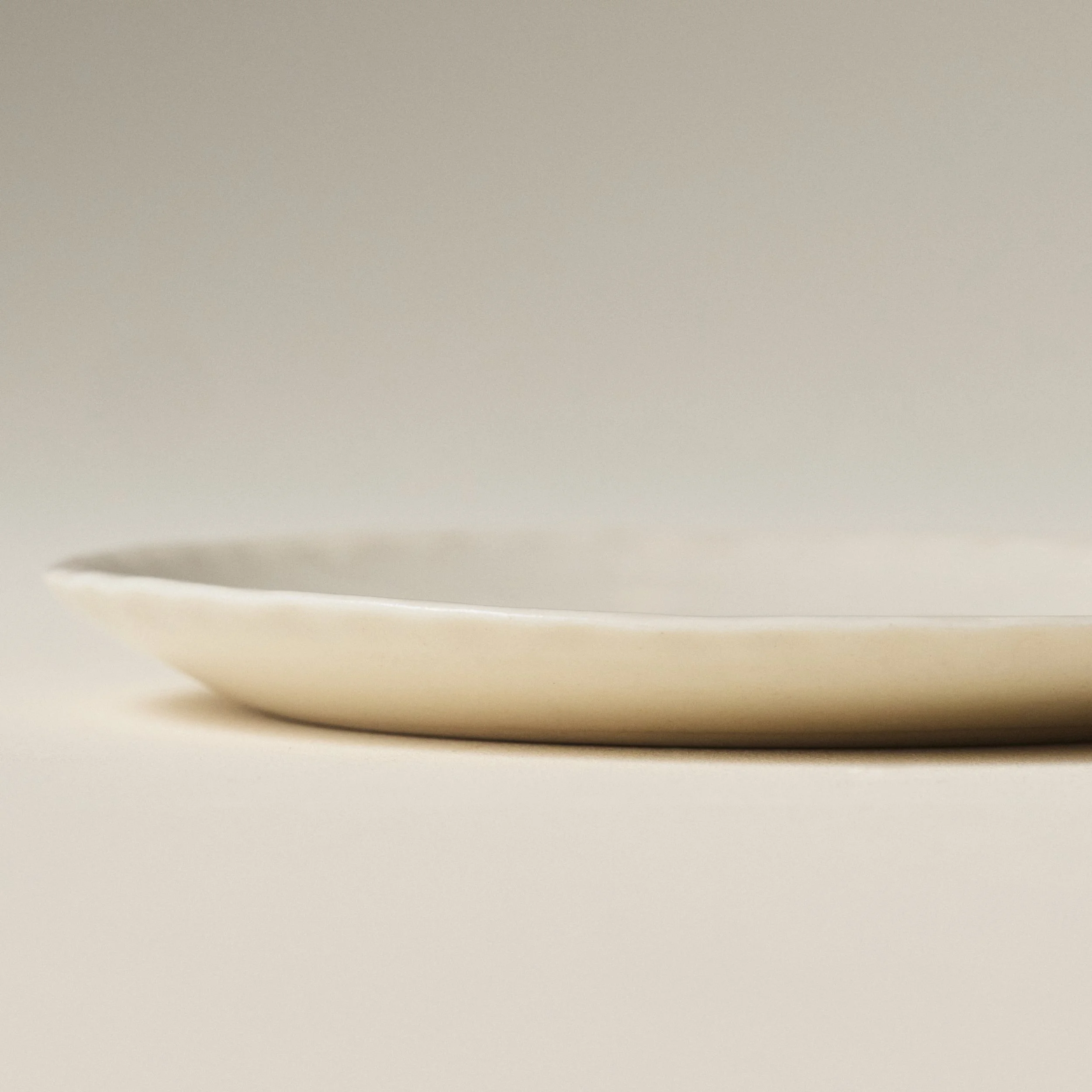 Side view of the PetitFelts Natural small ceramic plate showing its fluted rim