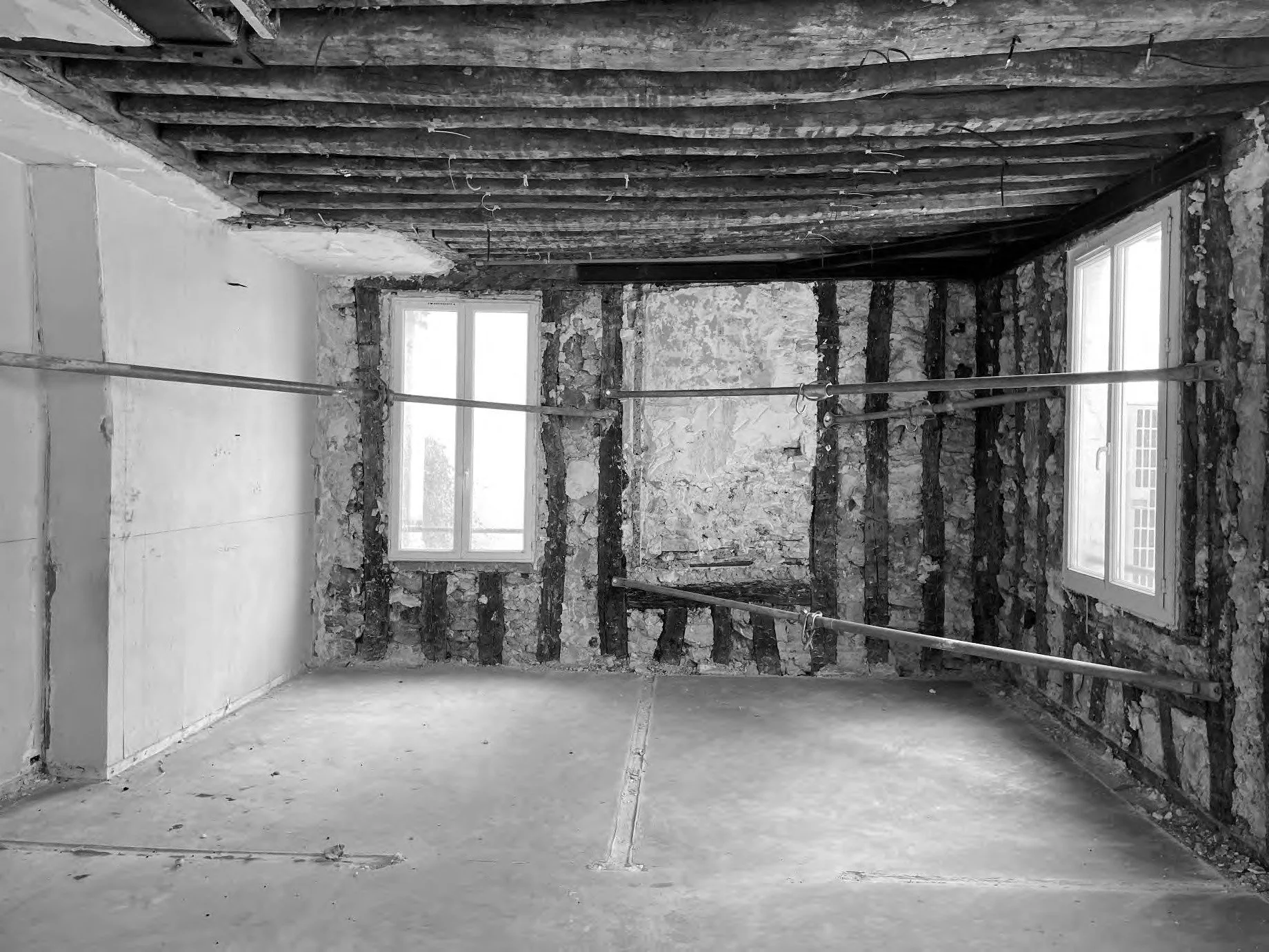 Room under renovation with exposed brick walls, two windows, and scaffolding.