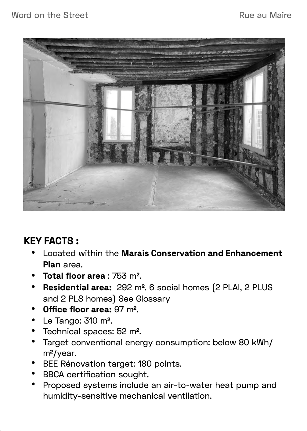 Black and white photo of an unfinished room with exposed beams on the ceiling, two windows, and walls with visible insulation and framing.